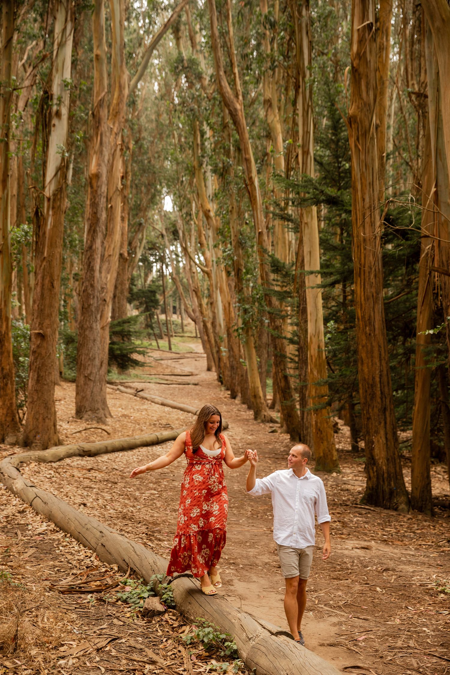 A couple walks together through a scenic eucalyptus grove trail covered in fallen leaves and dappled sunlight.