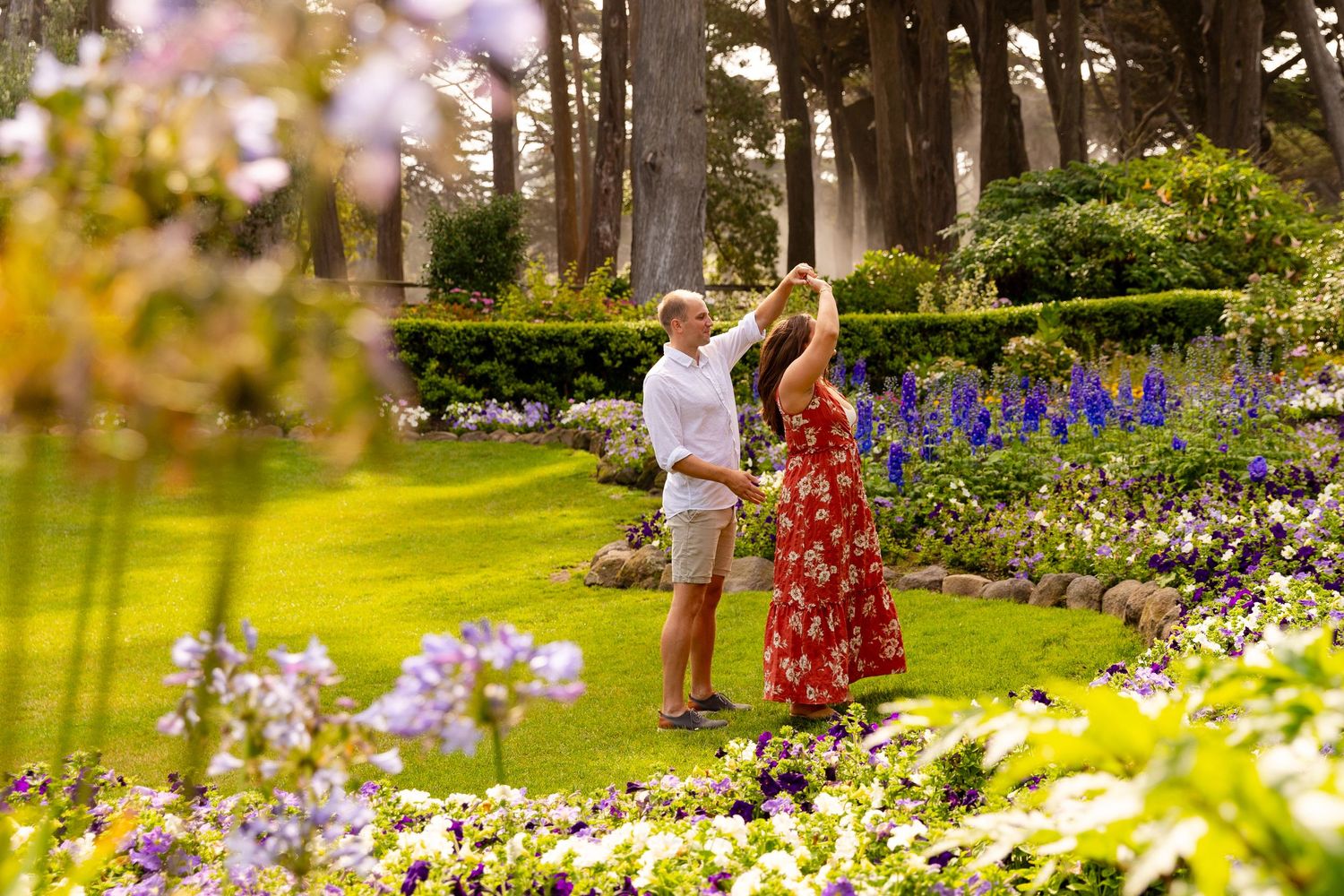A couple walks through a vibrant garden path with purple delphiniums and colorful summer flowers in bloom.