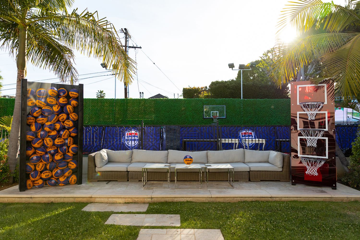 A basketball court with palm trees and colorful murals features multiple hoops and a concrete playing surface.
