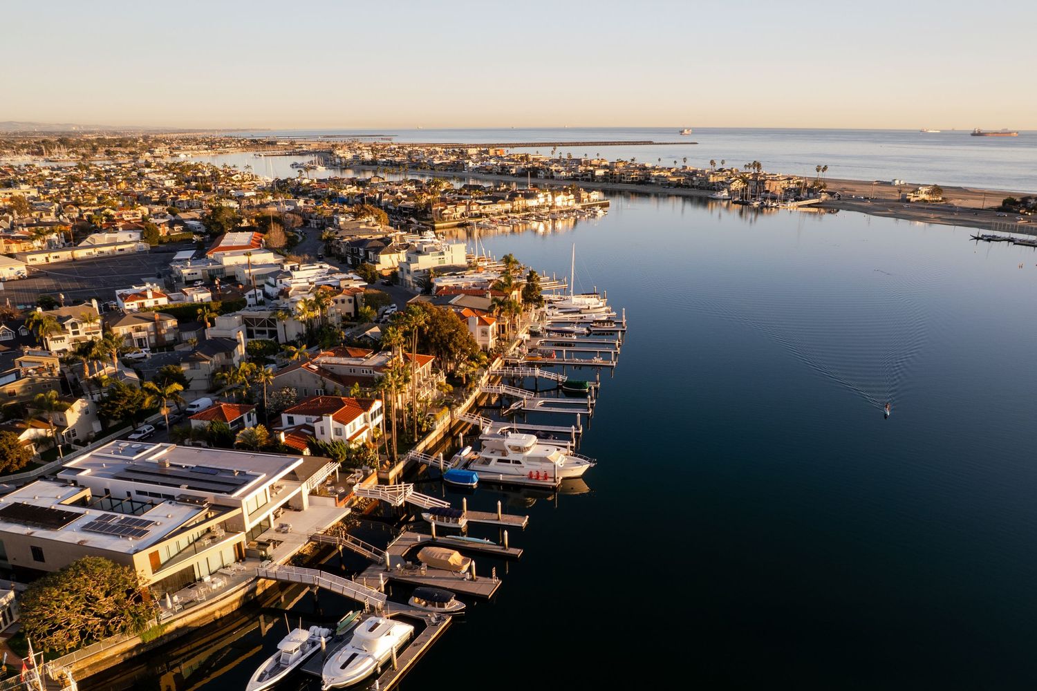 Aerial photography of a Long Beach CA marina with boats docked along the waterfront and residential buildings in warm sunset light.