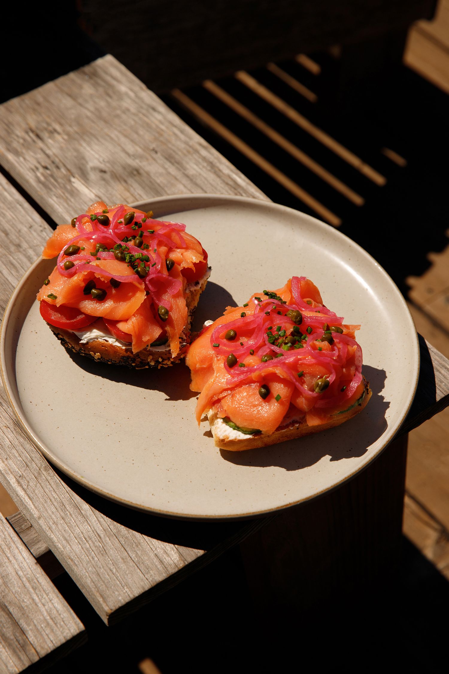 Two open-faced smoked salmon toasts with cream cheese and pickled red onions on a ceramic plate outdoors.