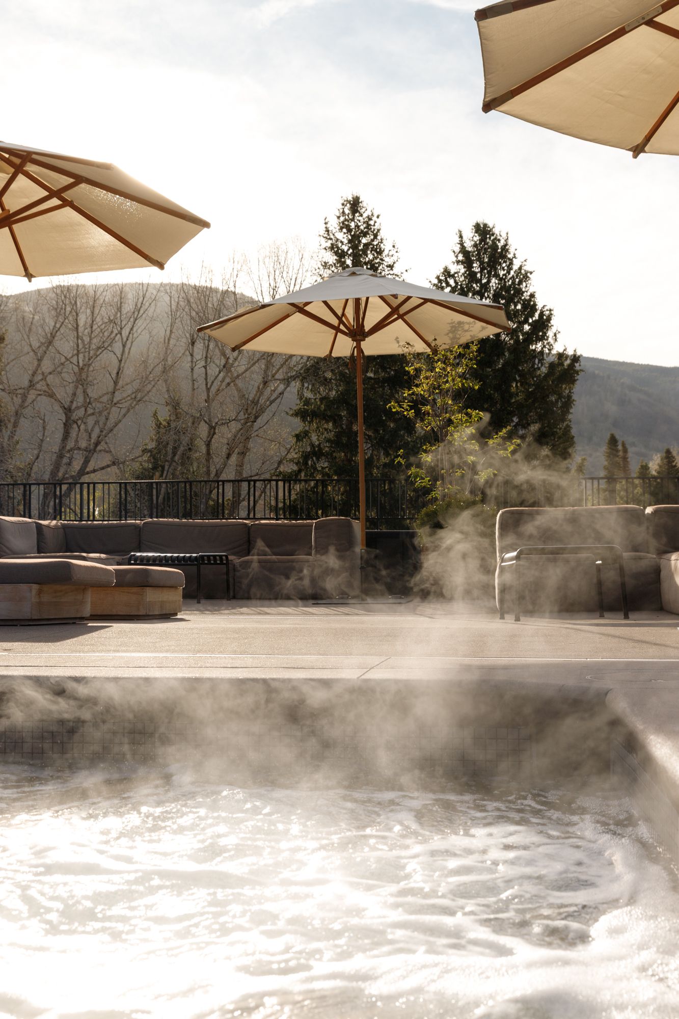 Steam rising from a hot tub at an upscale mountain resort with beige umbrellas and scenic views.