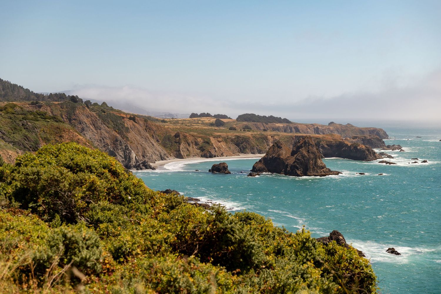 Panoramic view of rugged California coastline with dramatic cliffs and crashing waves against rocky shores.