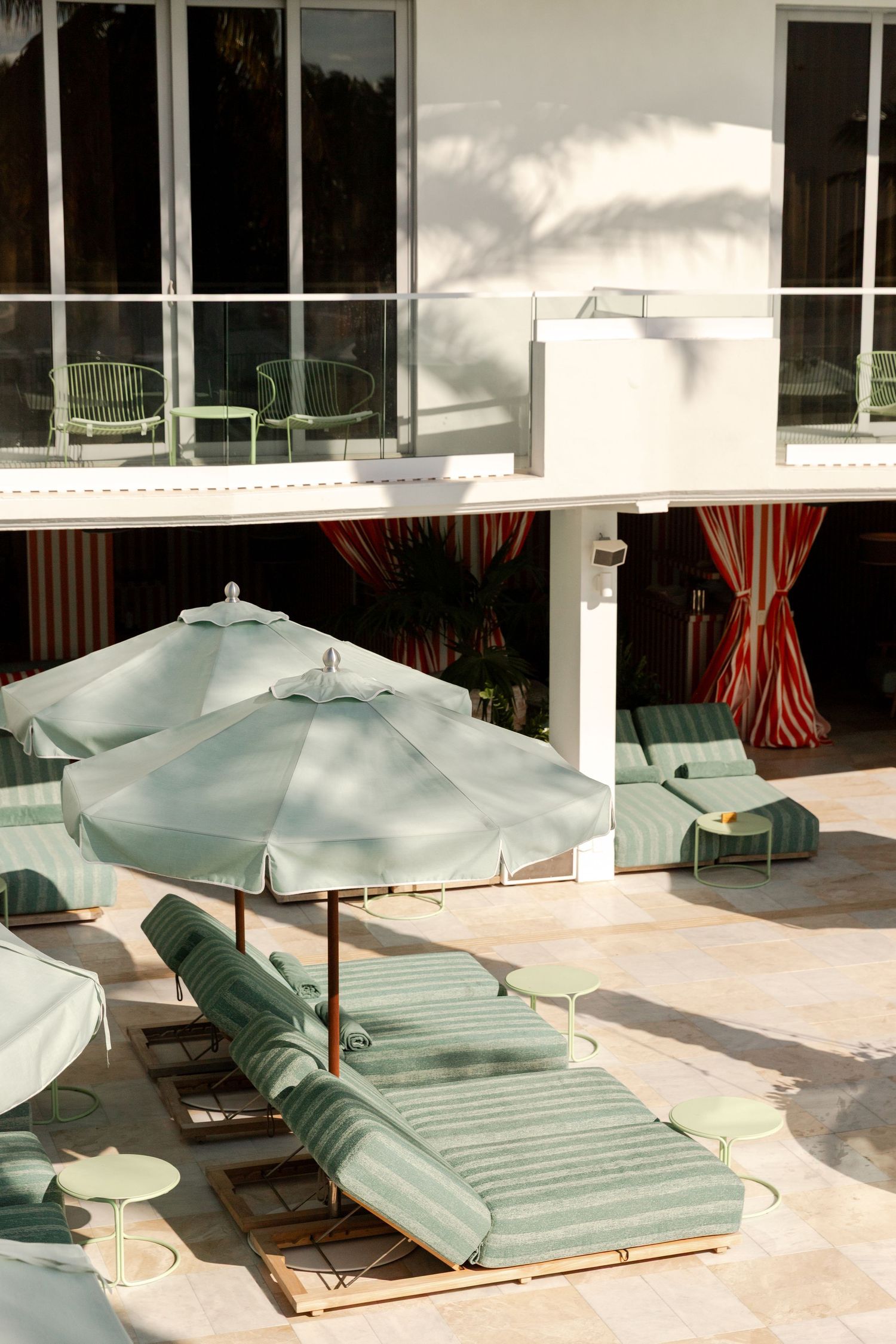 Green lounge chairs and umbrellas on a sunny patio deck with white columns and windows in the background.