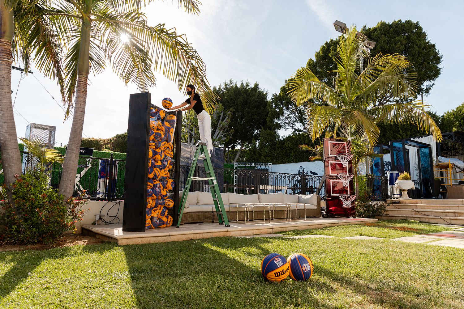 A panoramic view of a backyard basketball court with palm trees and outdoor furniture at sunset.