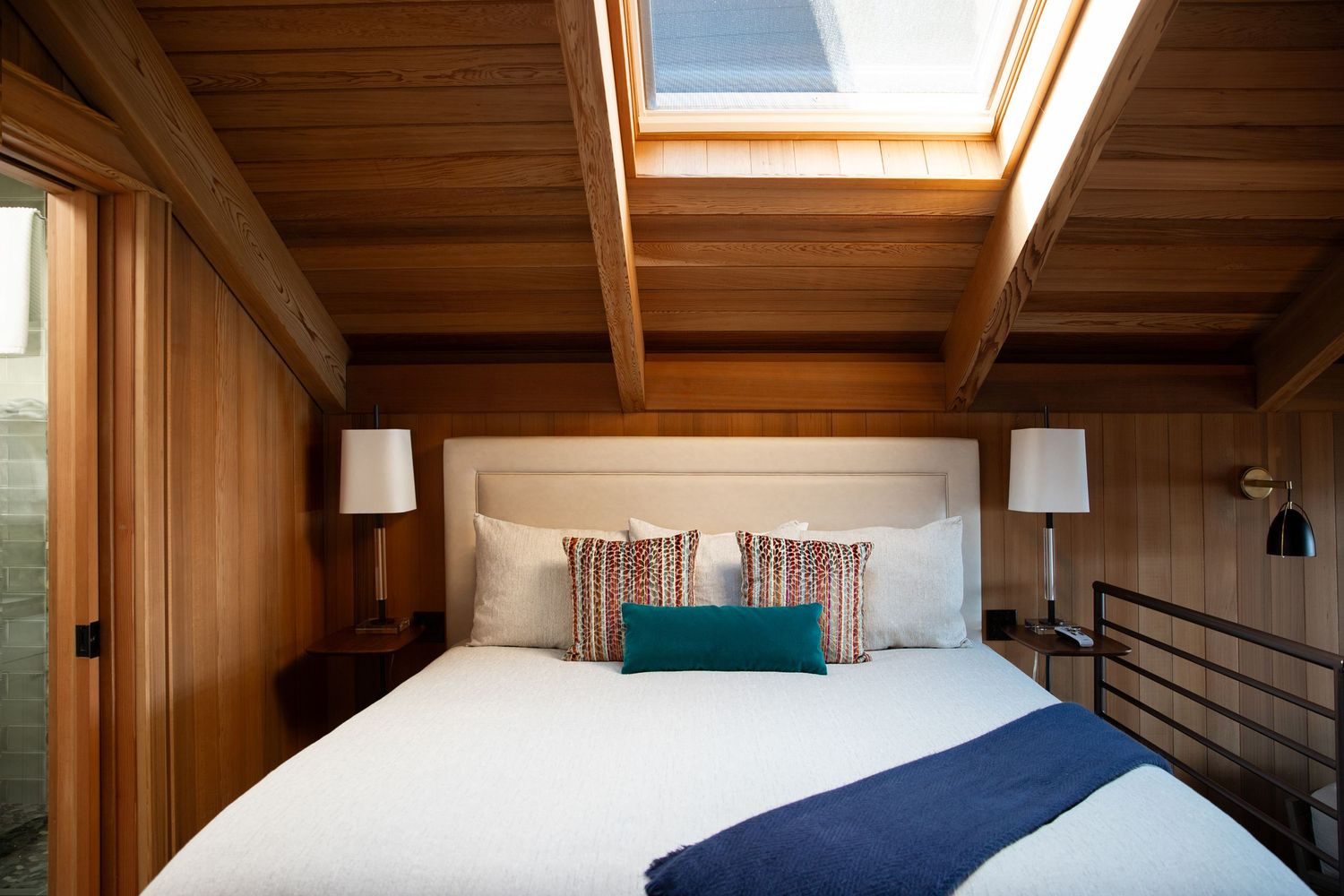 Modern bedroom interior with wooden beams and skylights letting in natural light.