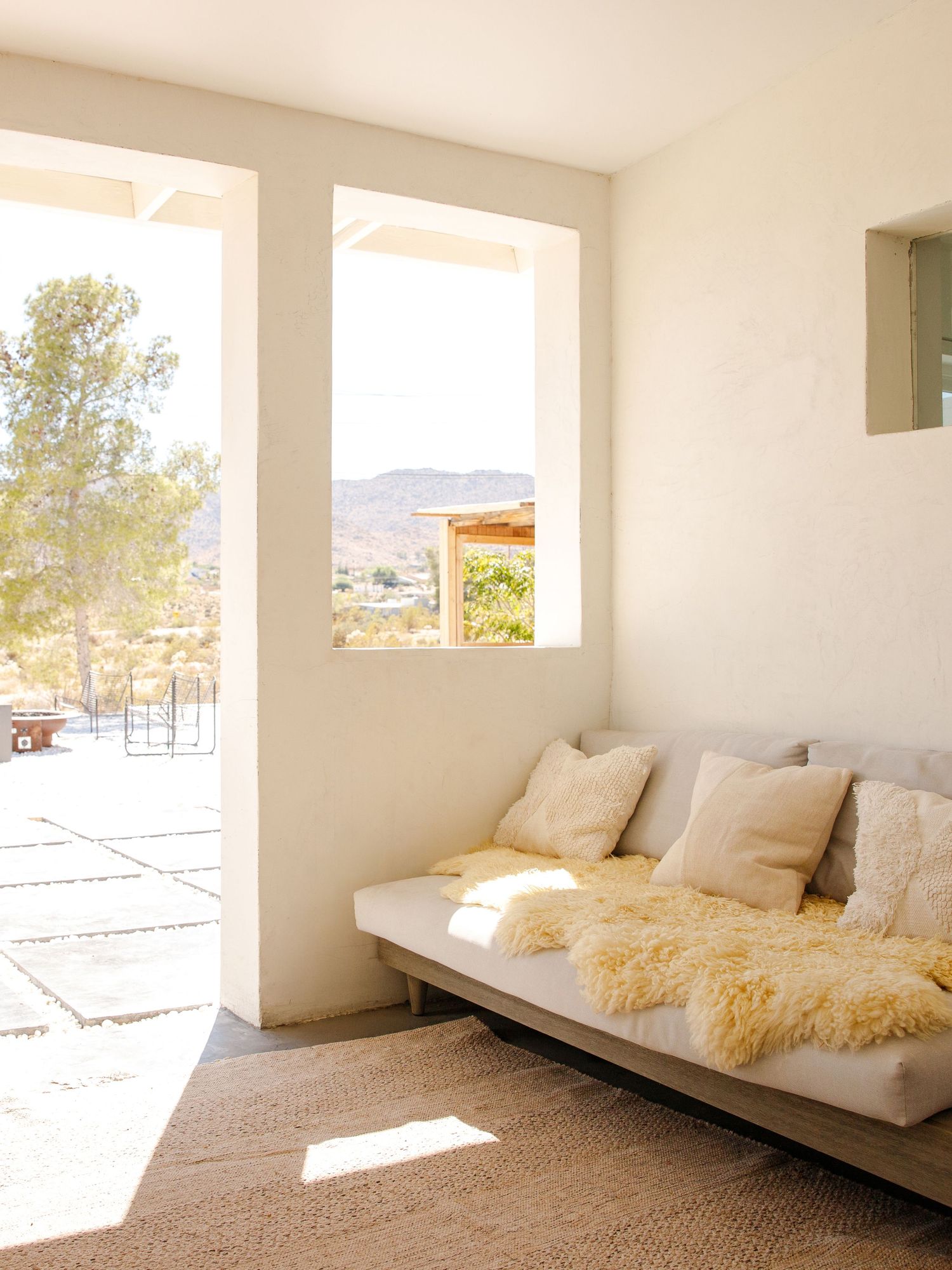 Minimalist white living room with a gray sofa, fluffy pillows, and desert mountain views through large windows.