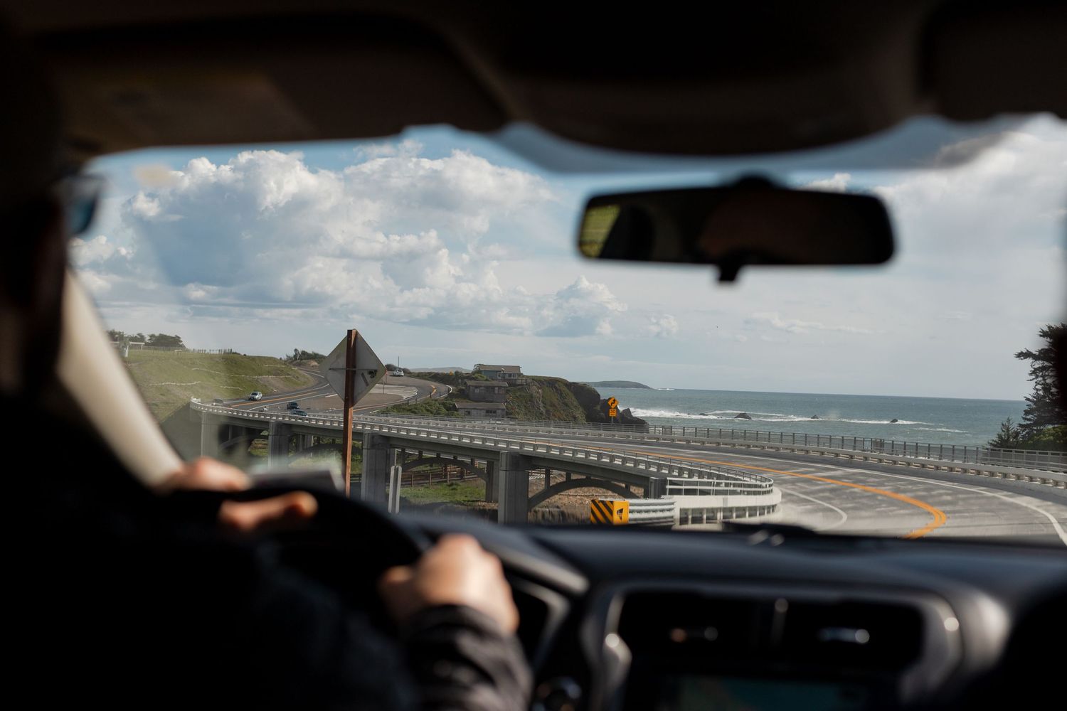 Travel photography editorial image of car driving along a scenic PCH in California with dramatic cliffs and ocean views.