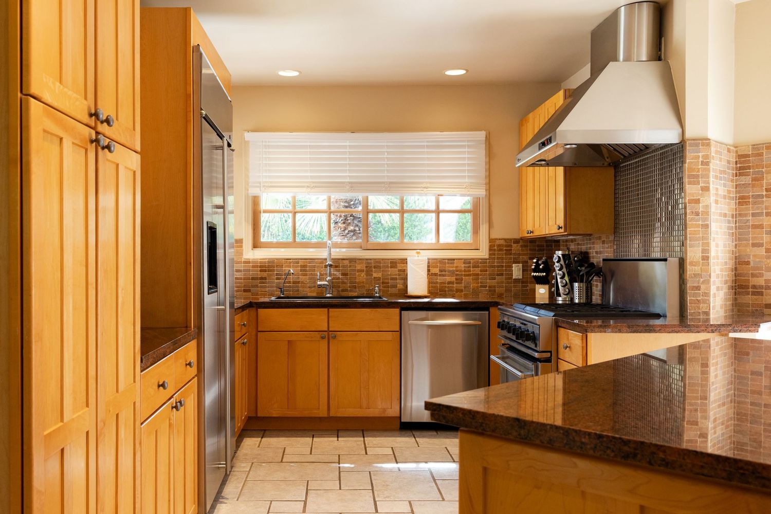 Modern kitchen with honey oak cabinets, granite countertops, stainless steel appliances, and brick backsplash tile flooring.