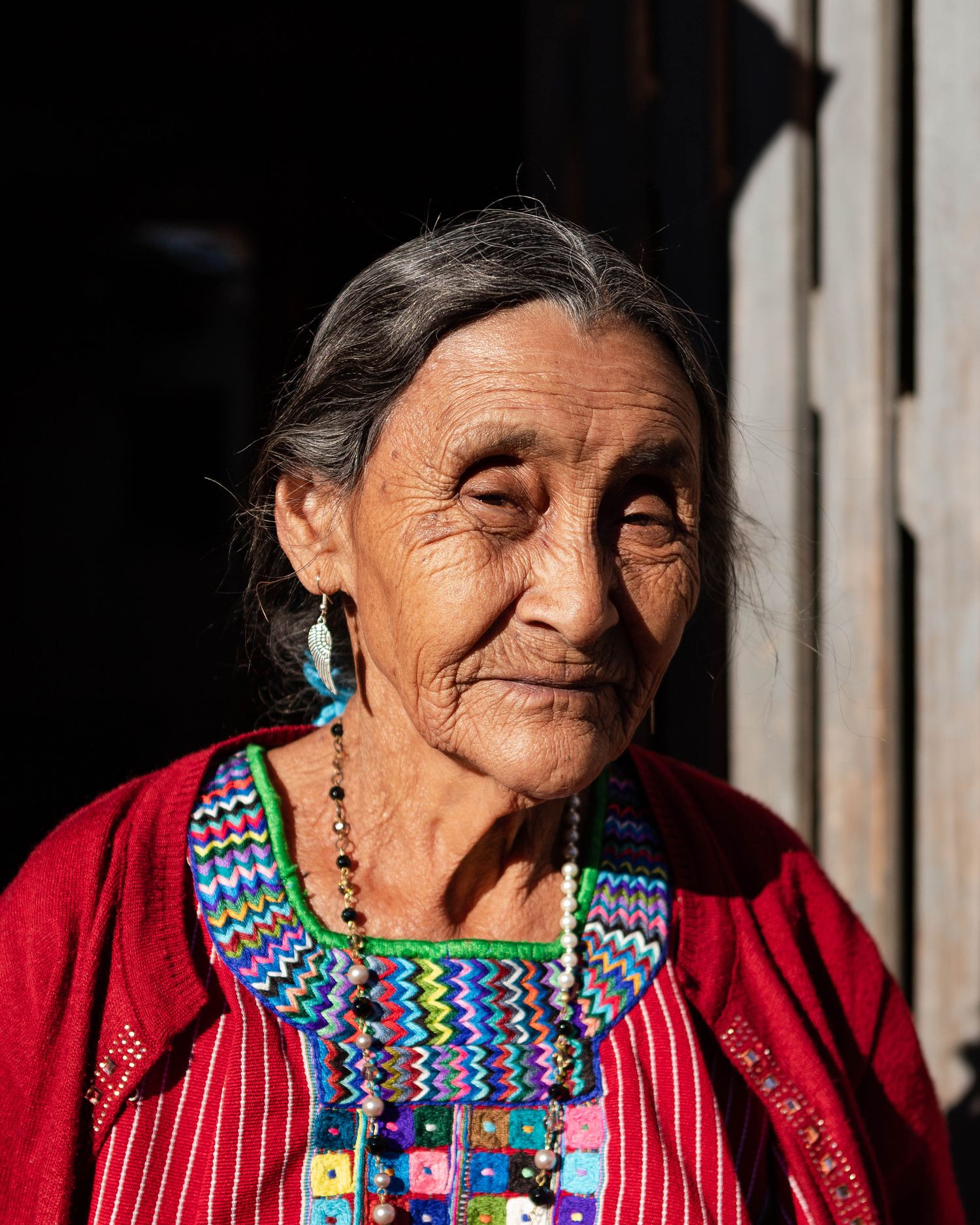 Editorial Image of a traditional textile artisan Guatemalan wearing colorful embroidered clothing in dramatic lighting.
