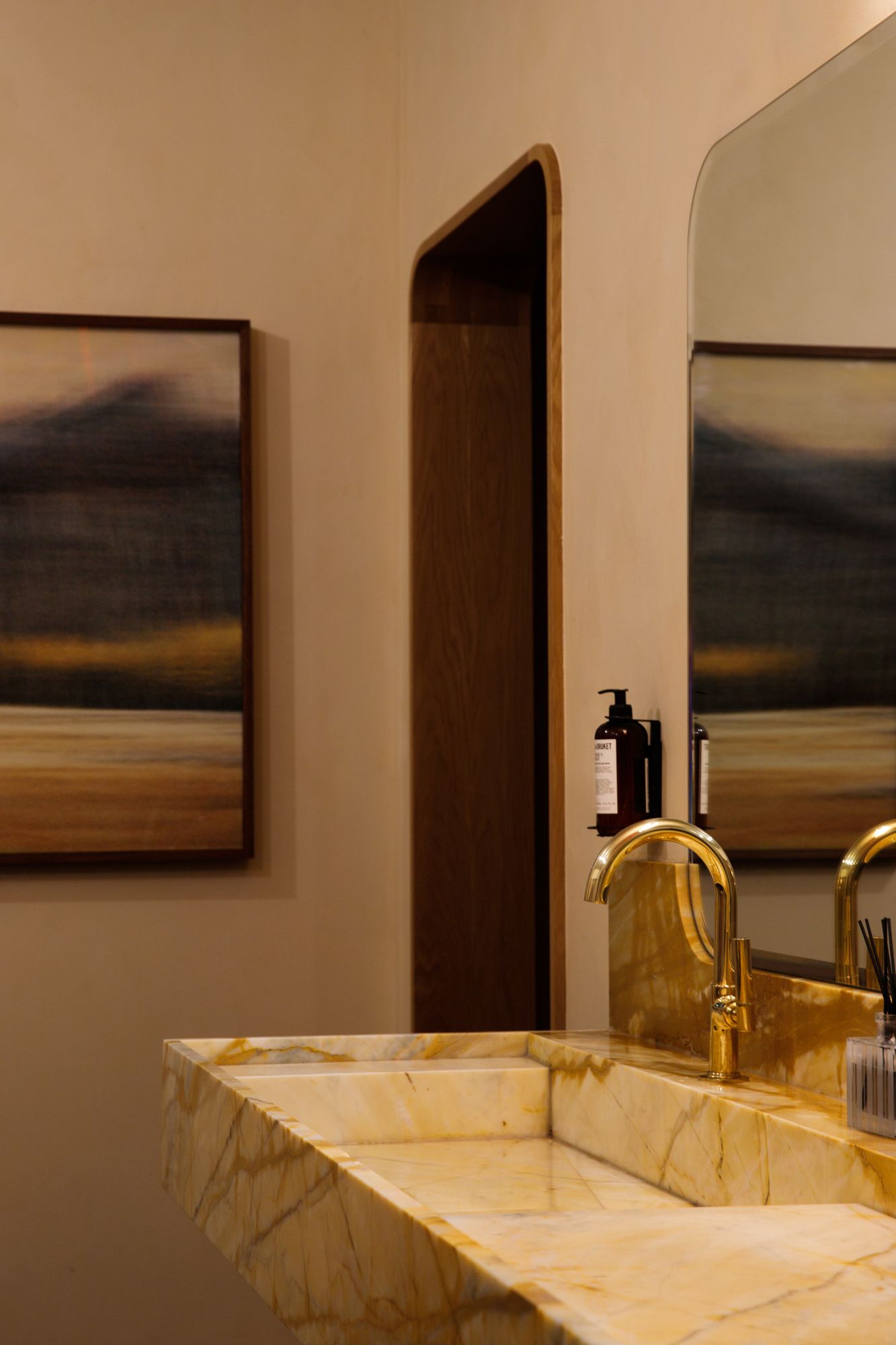 Luxury bathroom with golden marble sink, brass faucet, large mirror, and abstract landscape artwork.