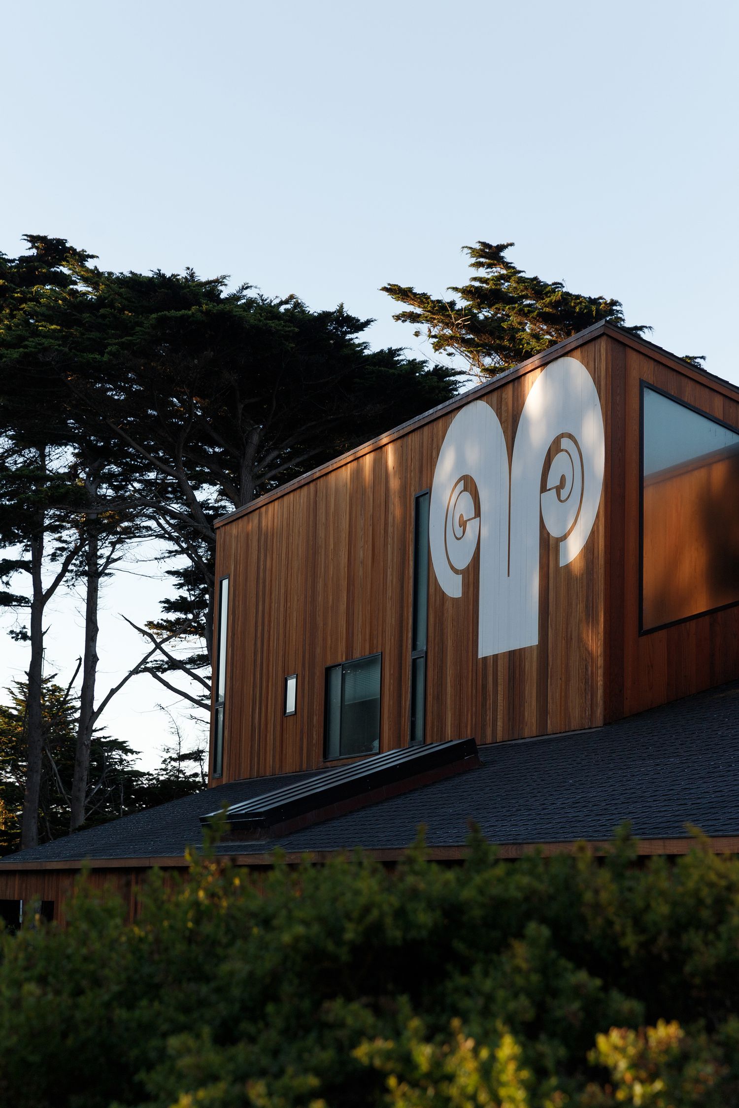 Modern wooden building with white ram horn artwork on exterior, surrounded by trees at dusk.