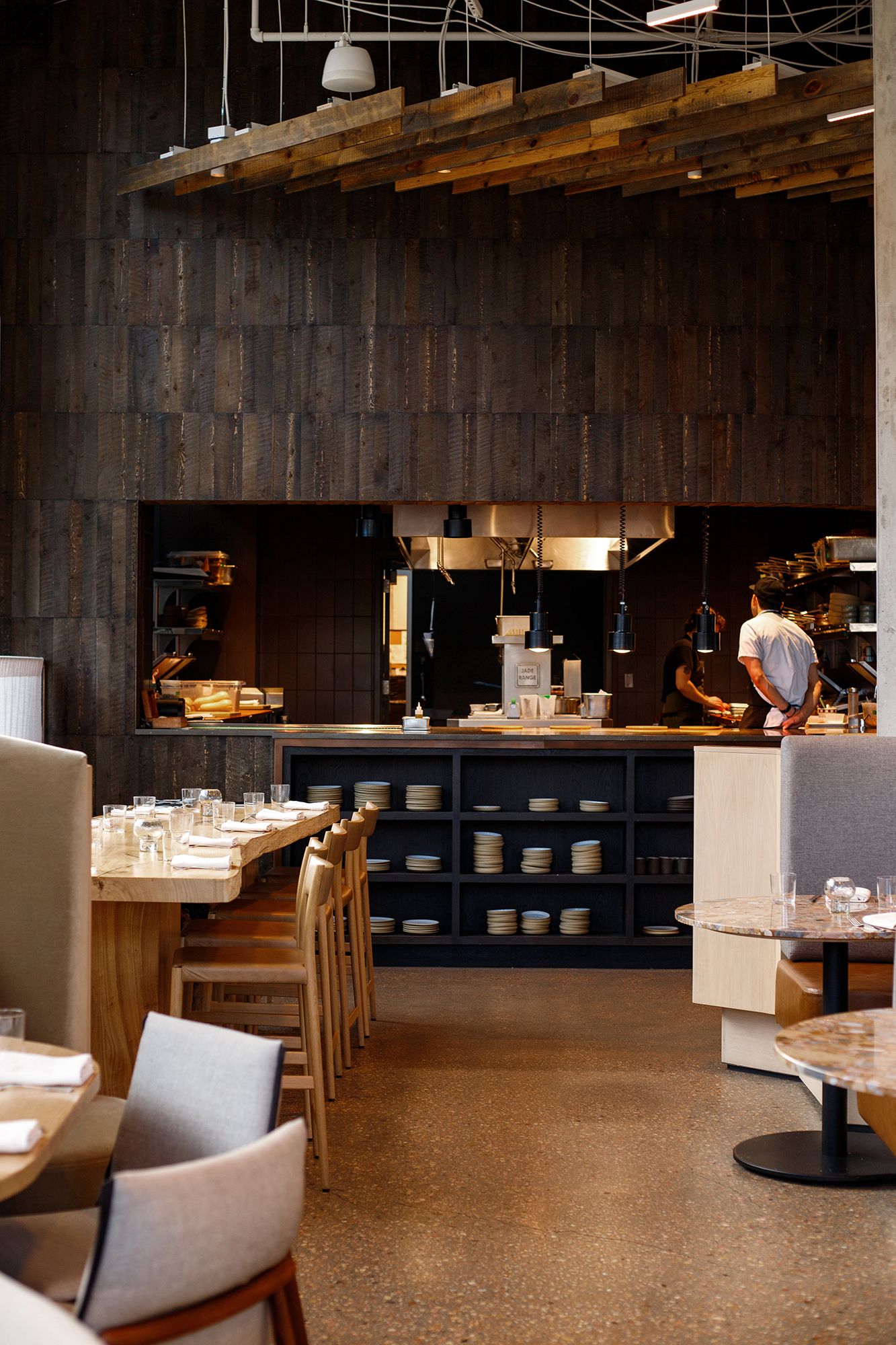 Modern restaurant interior with dark wood paneling, white tables, and upholstered chairs in a contemporary dining space.