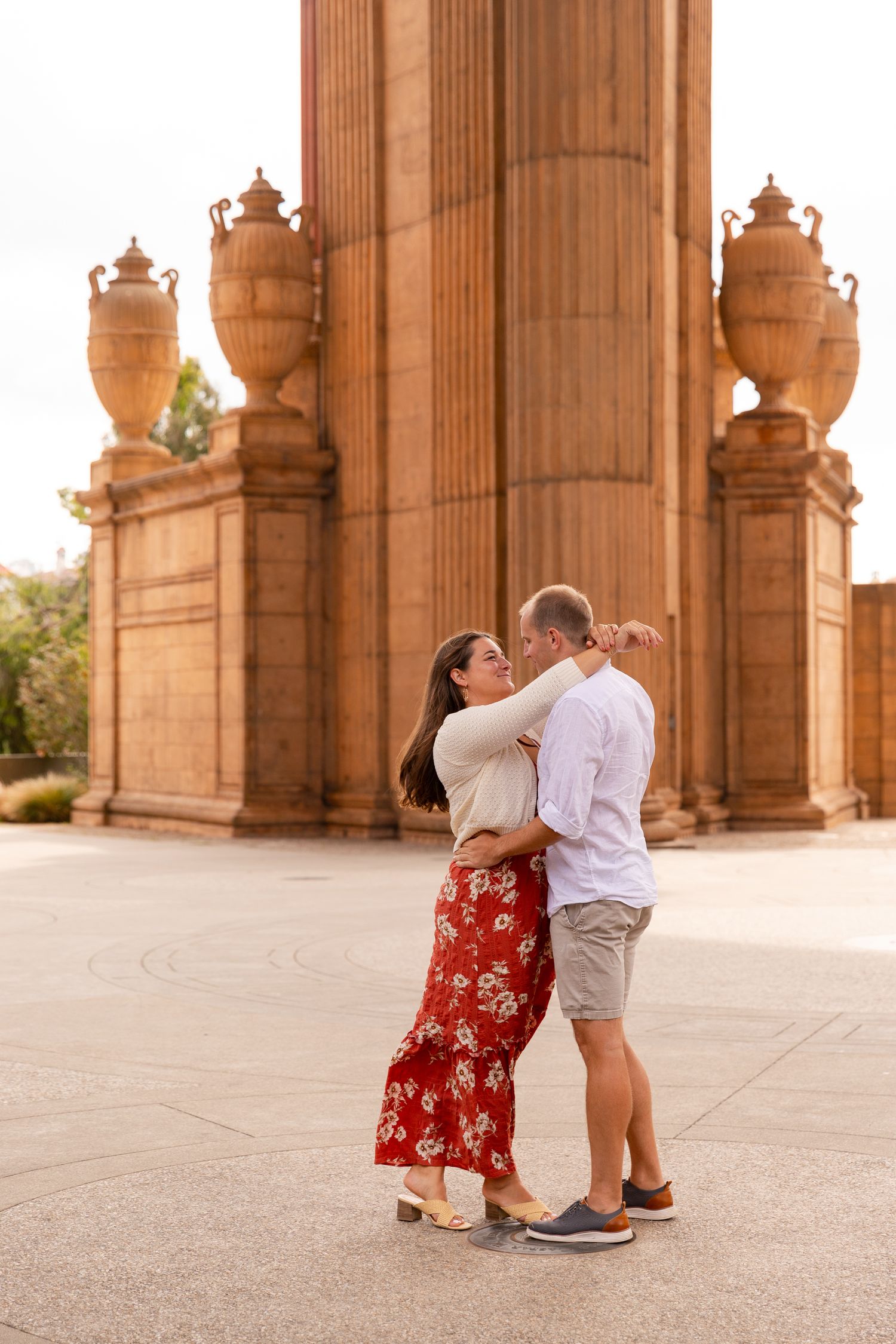 A couple shares a romantic moment under ornate stone archways at sunset in a beautiful architectural setting.