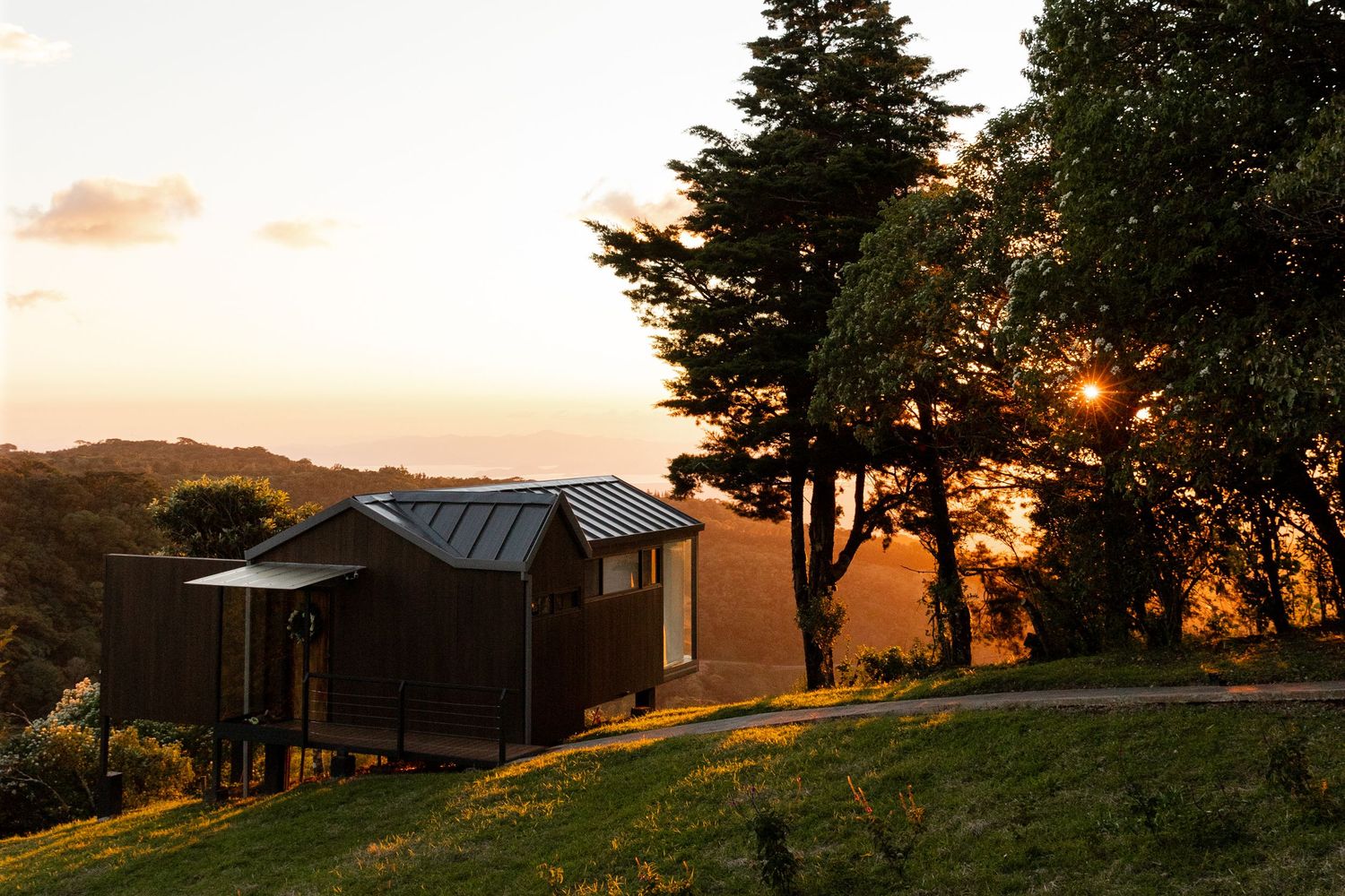 Rustic barn and evergreen trees silhouetted against a warm orange sunset sky in the countryside.
