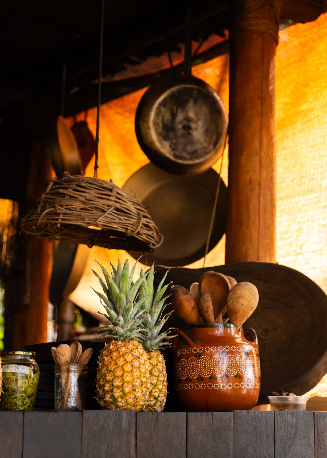 Editorial Travel Photography of a Rustic kitchen shelf with fresh pineapple and clay pot against warm-lit orange wall.