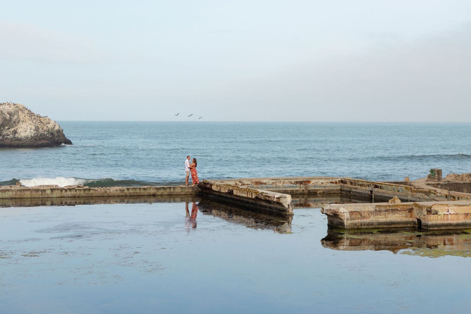 People exploring the historic Sutro Baths ruins along the rocky San Francisco coastline during low tide.