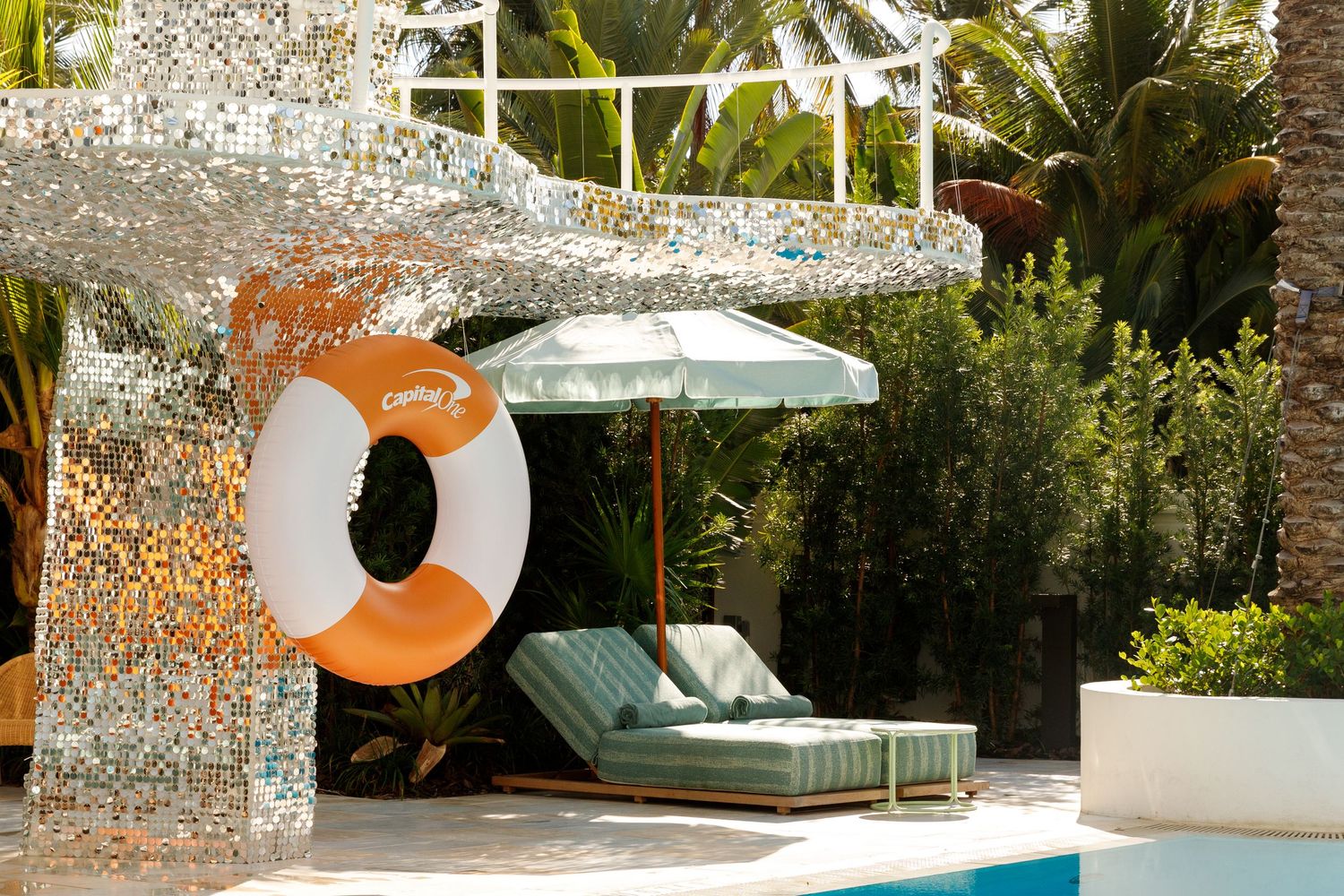 A modern outdoor swimming pool area with white lounge chairs and tropical landscaping features.