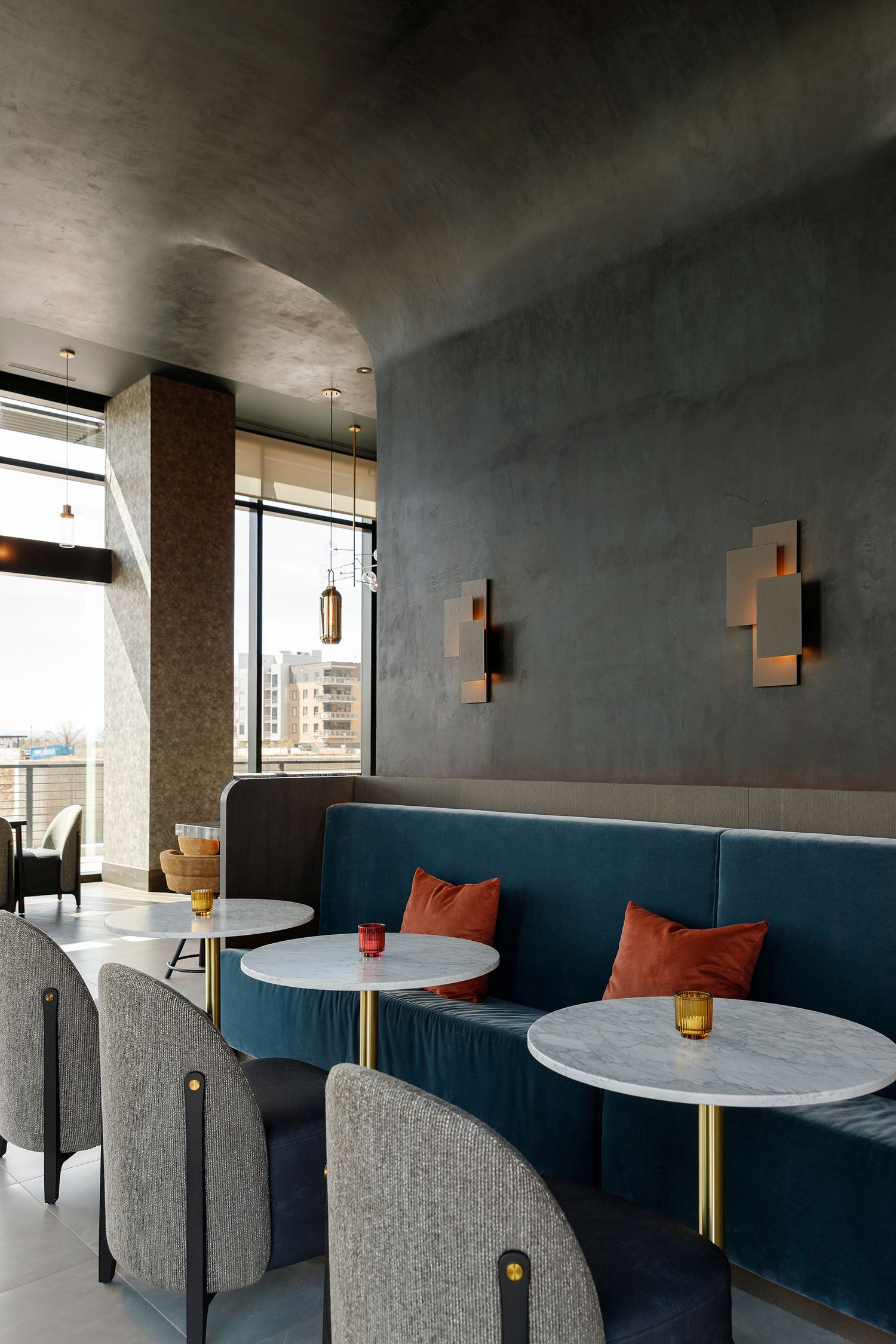 Restaurant lounge with teal velvet banquette, marble tables, rust throw pillows. Hospitality photographer in Denver, Colorado.