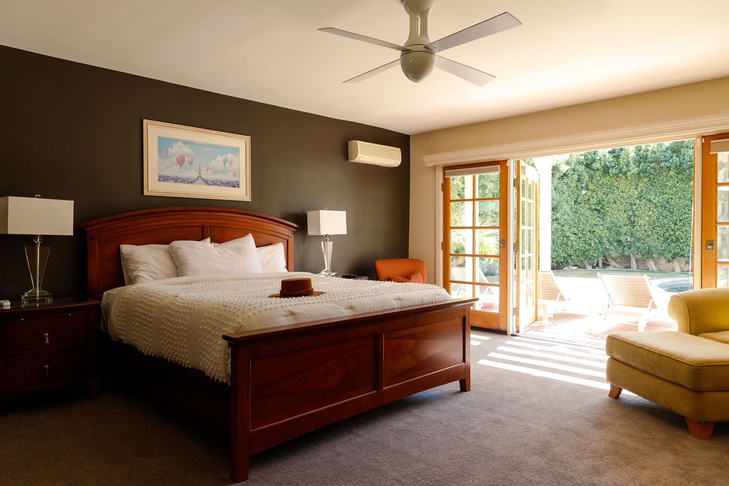 Elegant master bedroom with cherry wood bed, ceiling fan, French doors opening to garden, and wall-mounted AC unit.