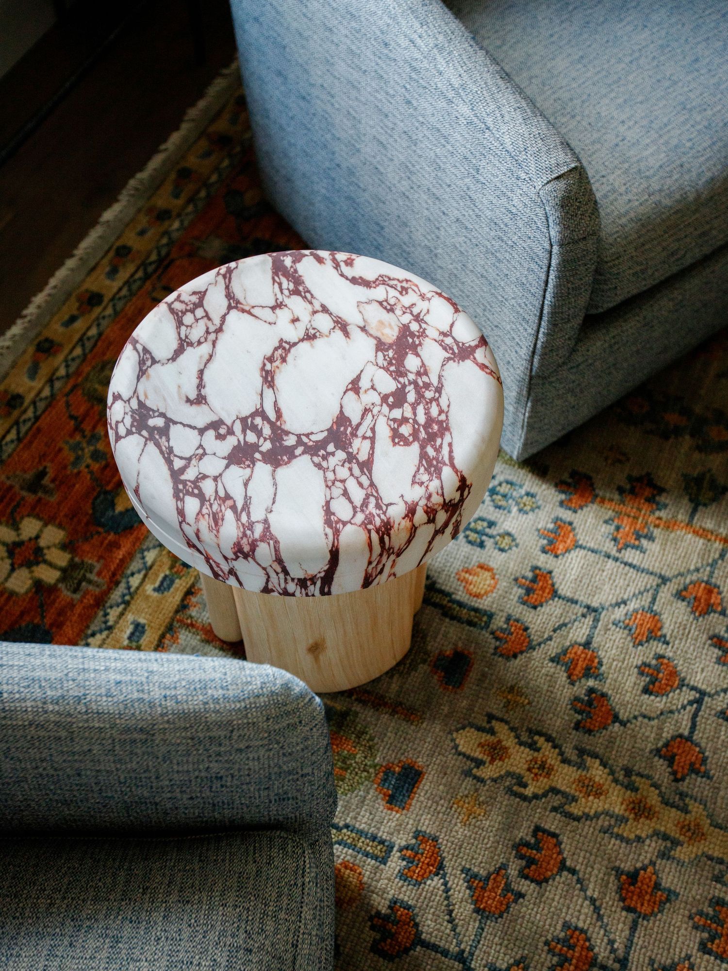Marble-topped wooden side table with red veining, placed between gray upholstered chairs on a patterned area rug.