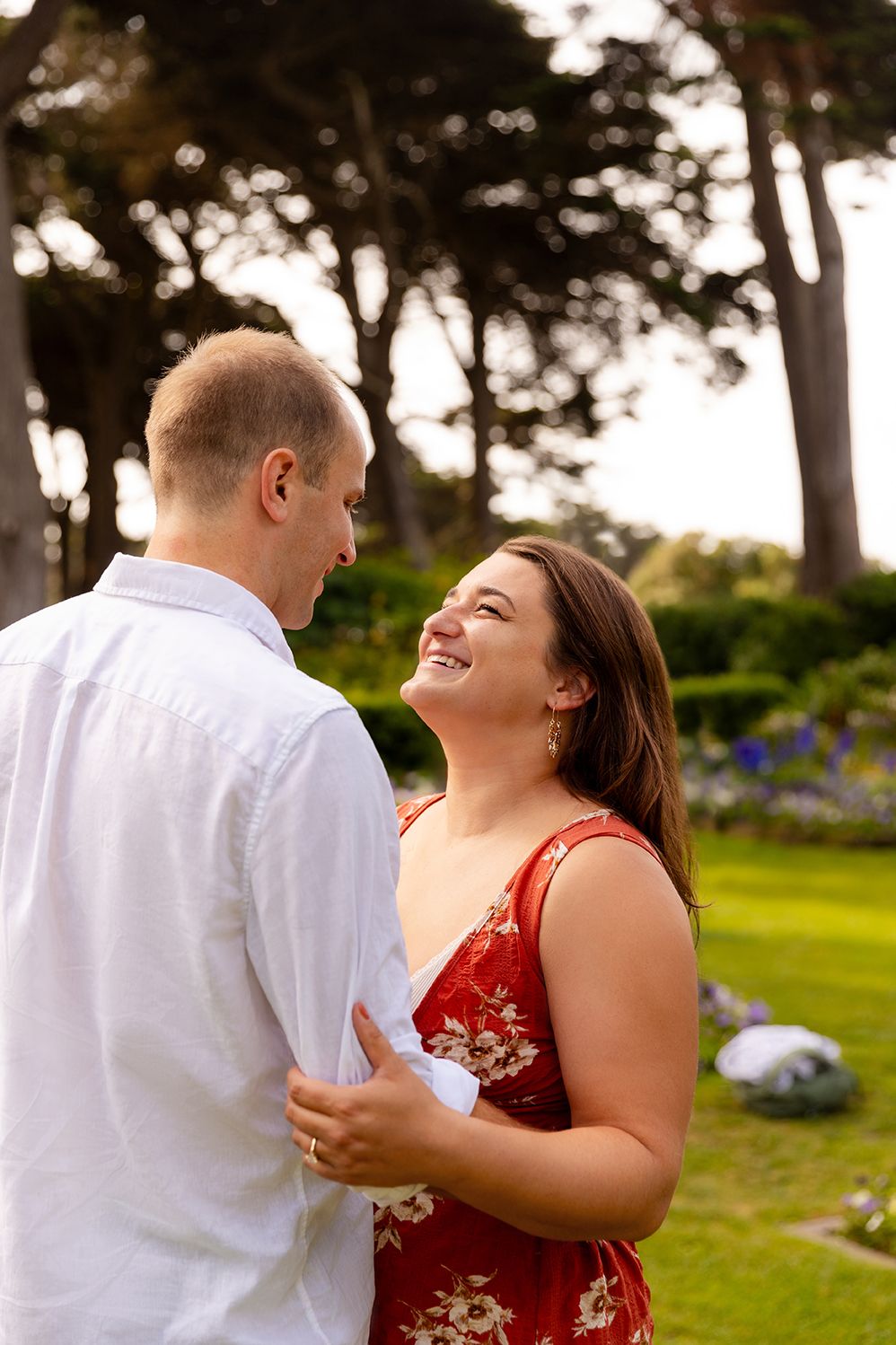 A couple shares a joyful moment together while dancing outdoors in a park setting at sunset.