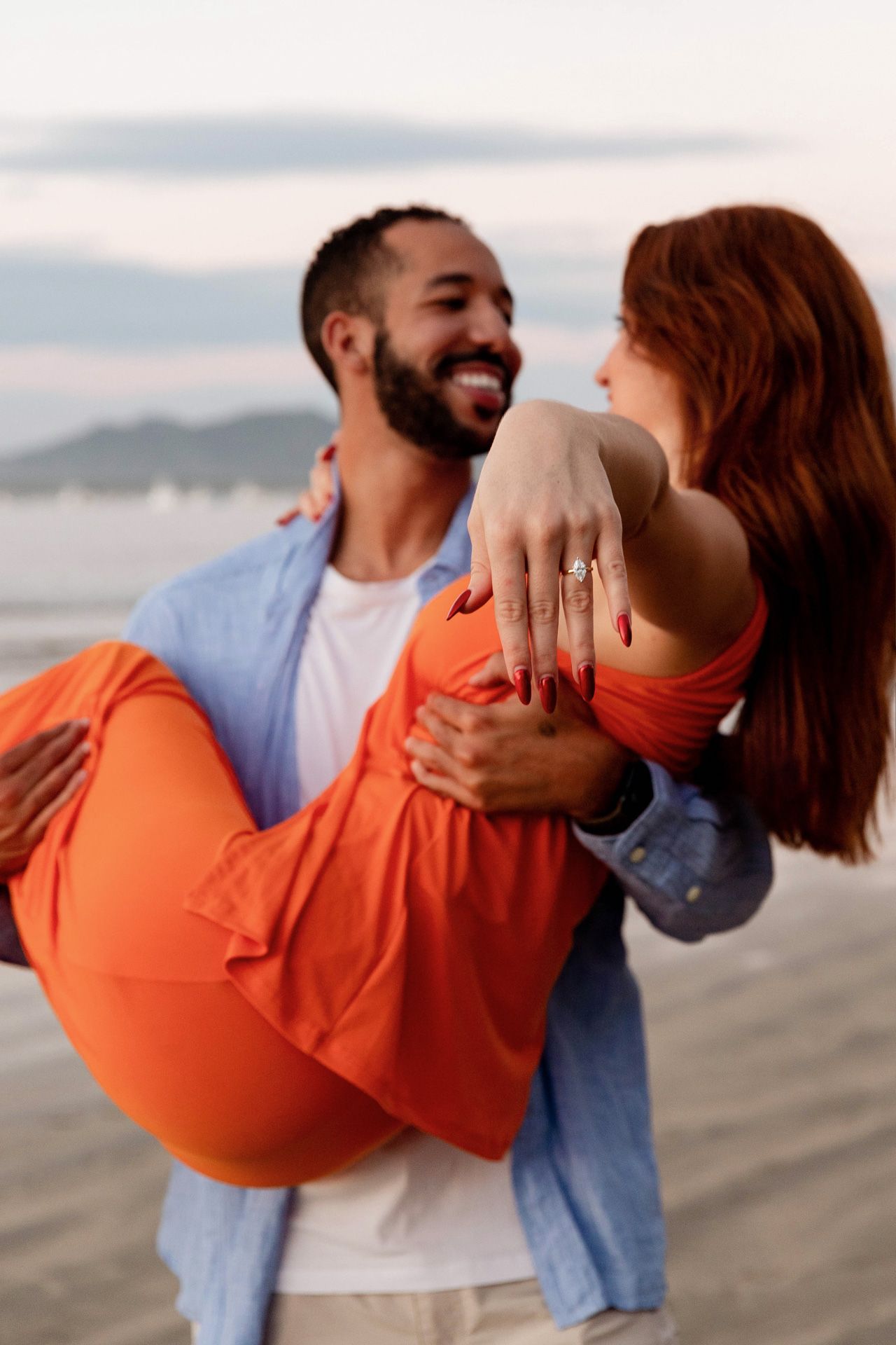 A playful couple in orange and denim sharing joyful moments on a beach.
