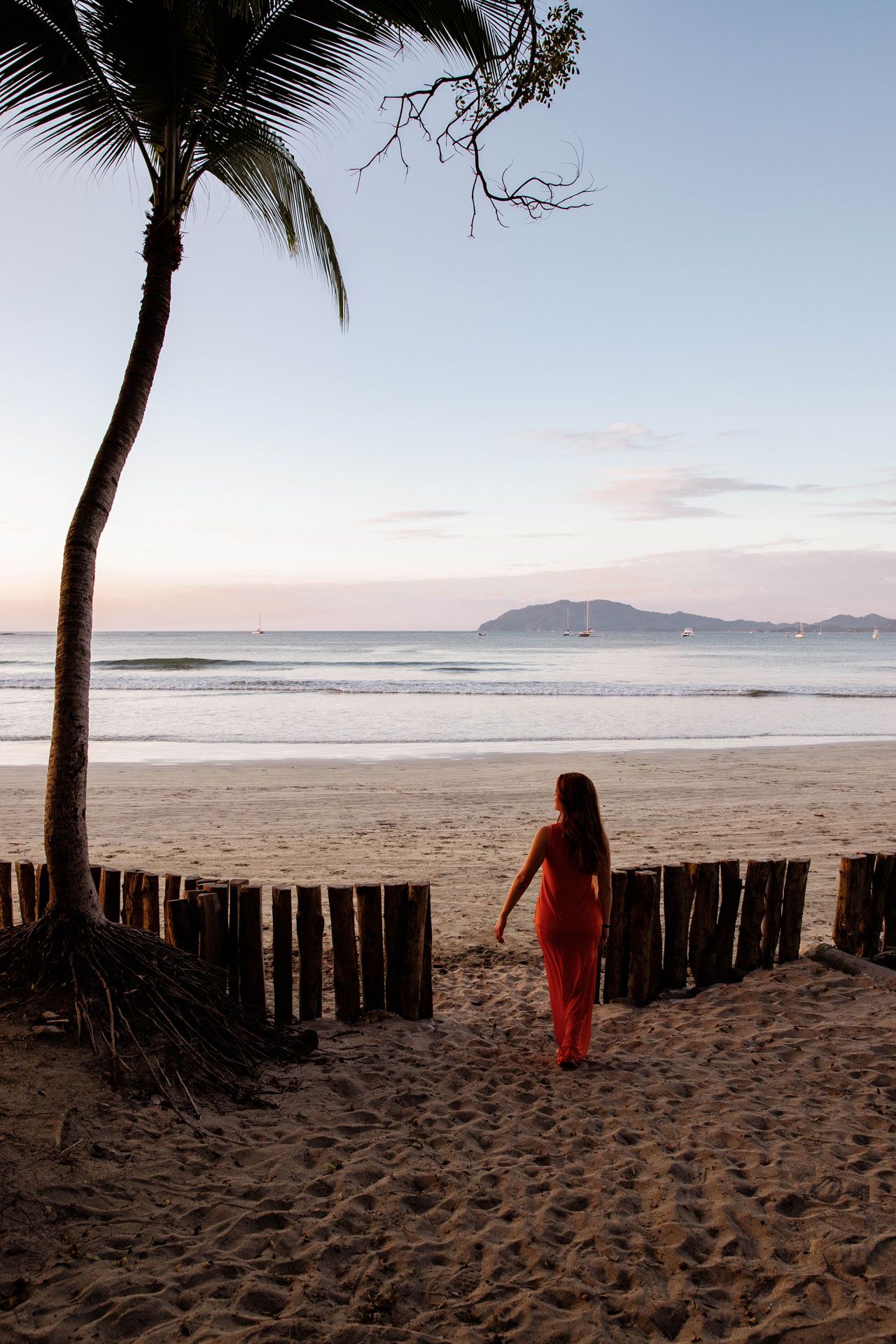 A series of five beach photos showing a wooden fence and palm trees at sunset with distant mountains on the horizon.