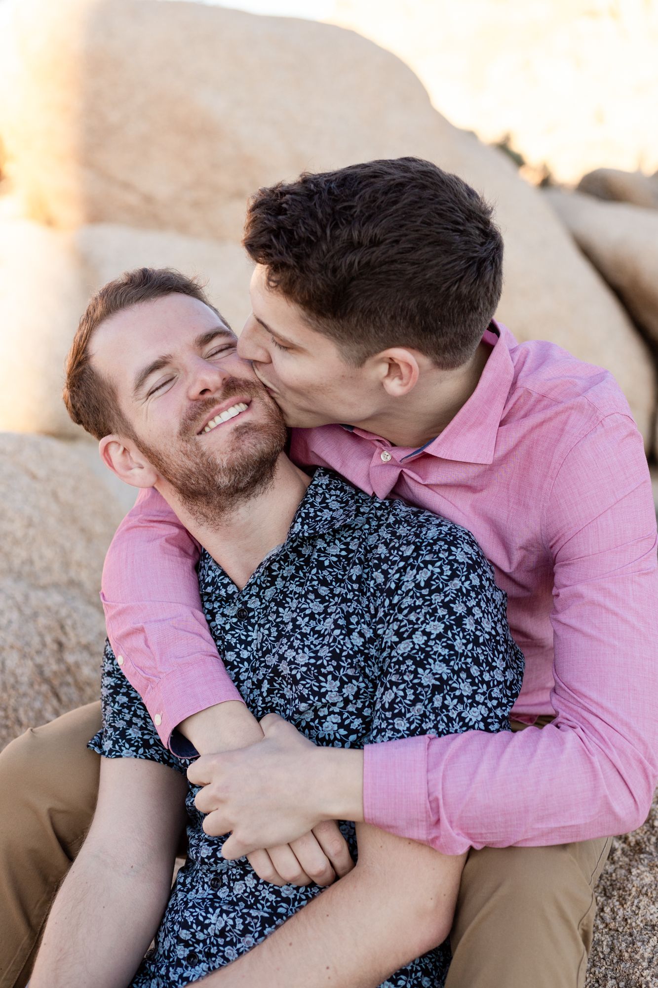 A couple sharing tender moments while sitting on rocks during an outdoor photoshoot.