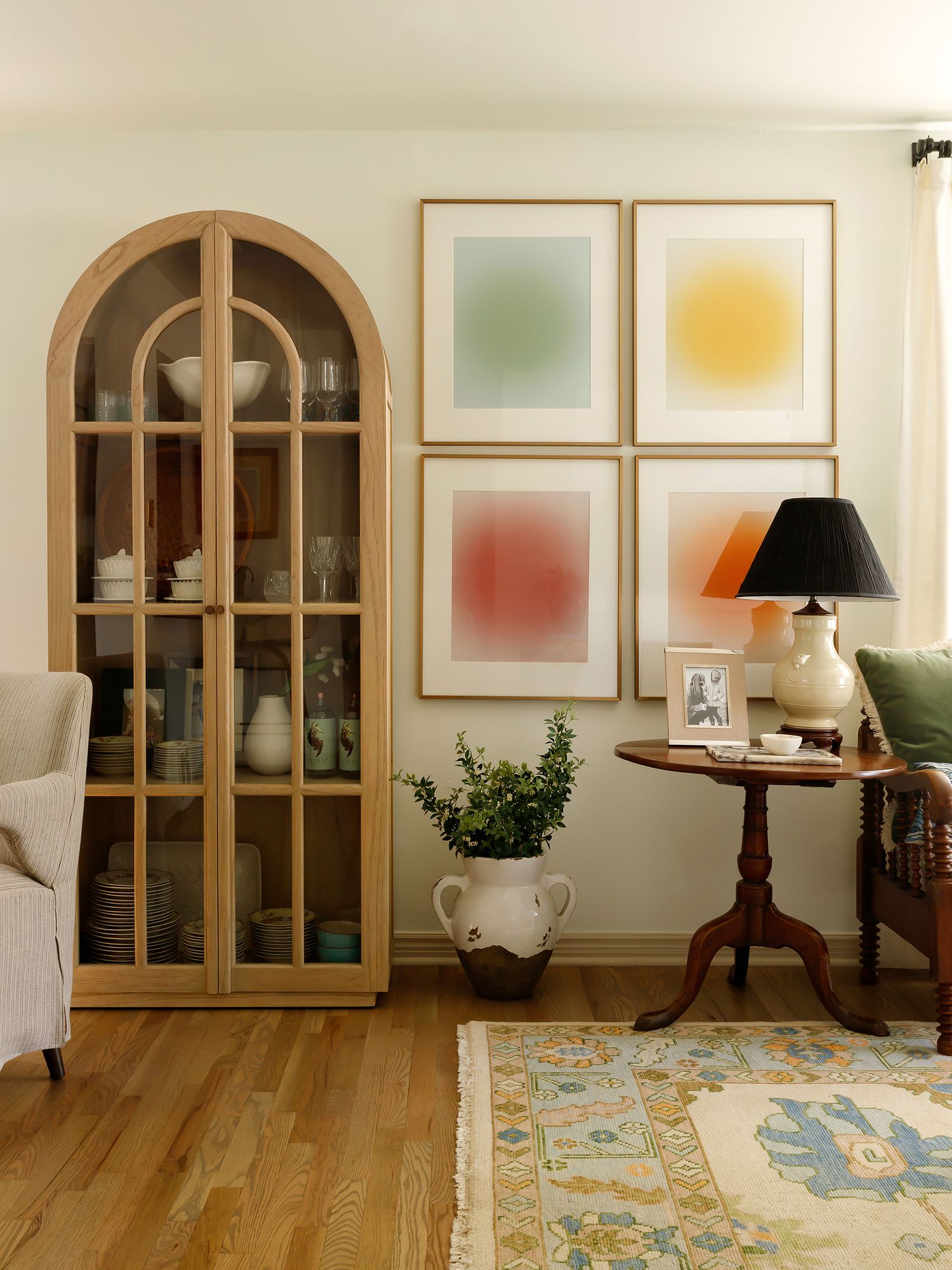 Cozy living room with arched wood cabinet, colorful abstract wall art, antique side table, black lamp, and vintage rug.
