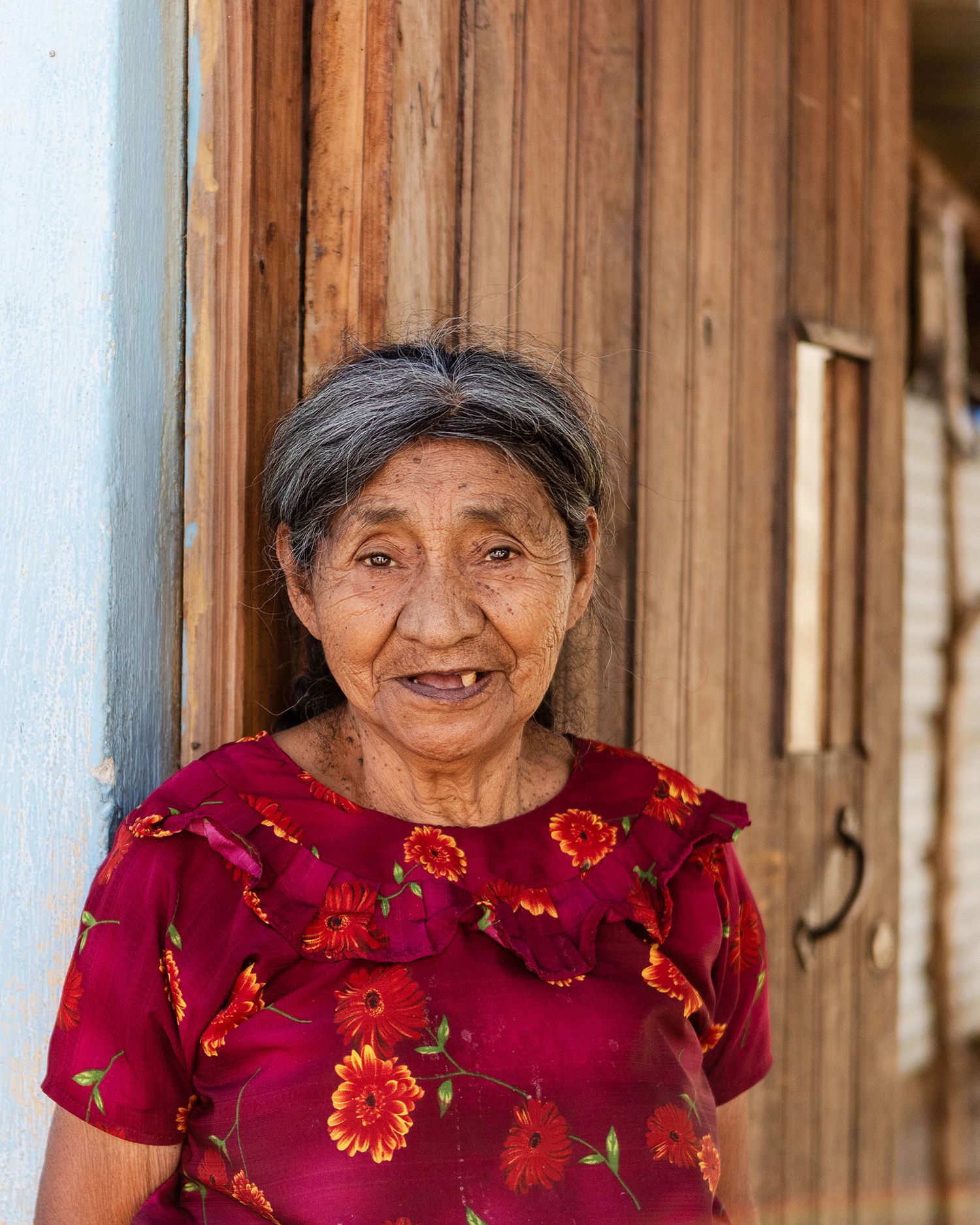 Editorial travel phogoraphy of Guatemalan woman with blue pillars and red floral decorative elements in the background