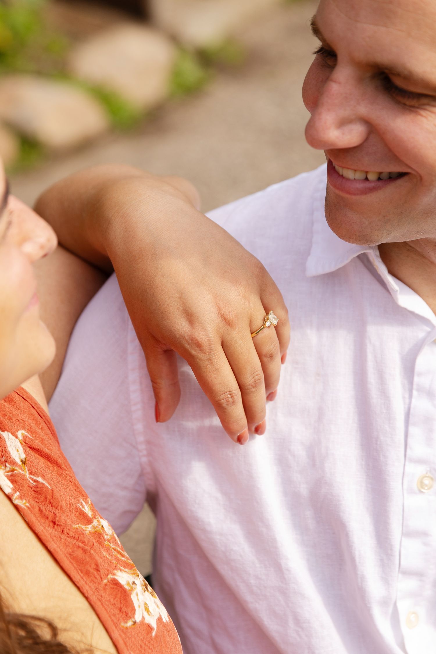 Close-up view of a couple showing a gold wedding ring on hand with person in white shirt smiling.