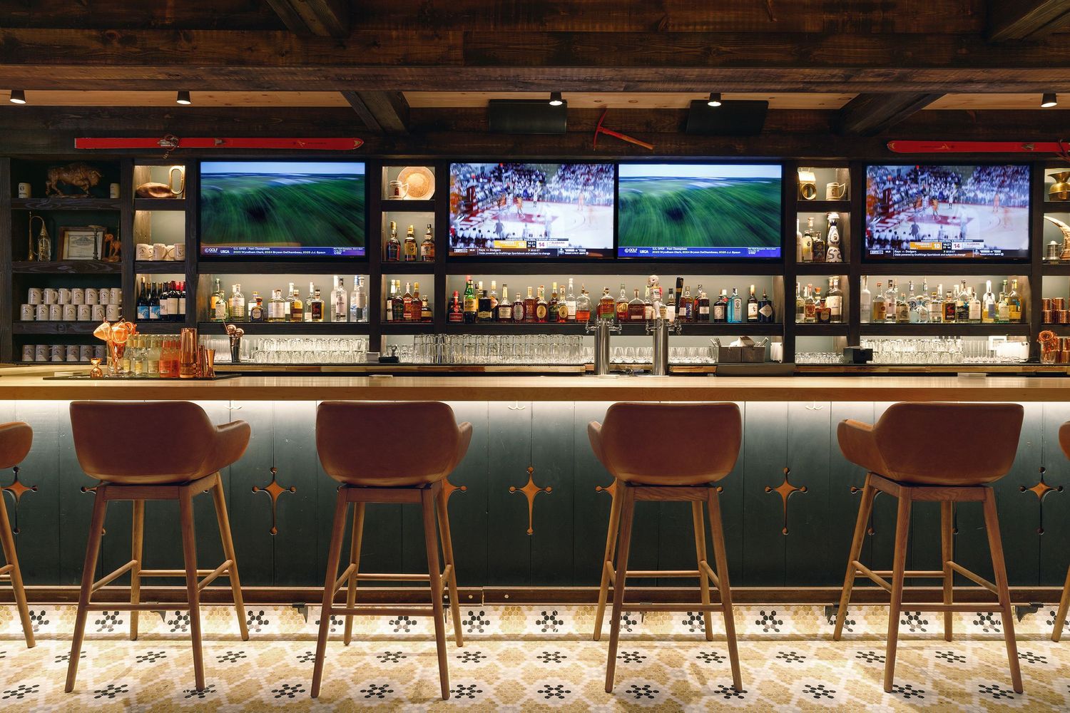 Elegant bar with teal counter, velvet stools, backlit shelves of spirits, and scenic TV displays above.