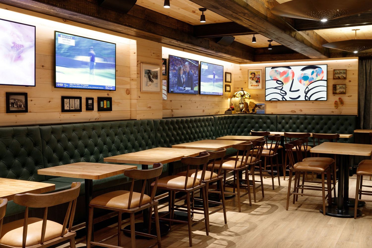 Sports bar dining area with green tufted booths, wooden tables, bar stools, and multiple wall-mounted TVs showing live sports.