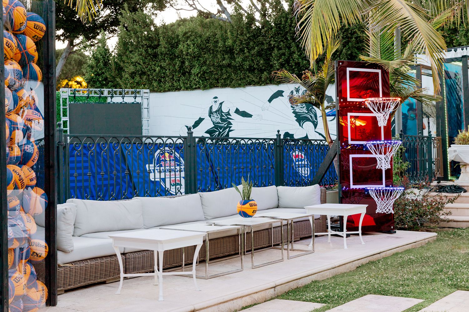 Outdoor patio space with white cushioned seating, wicker furniture, and tropical landscaping along a blue wall.