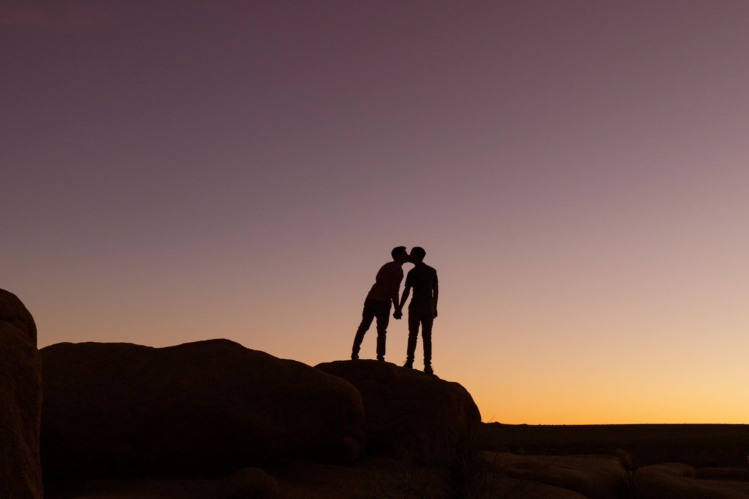 Silhouettes of people standing on a hilltop against a vibrant orange and purple sunset sky.