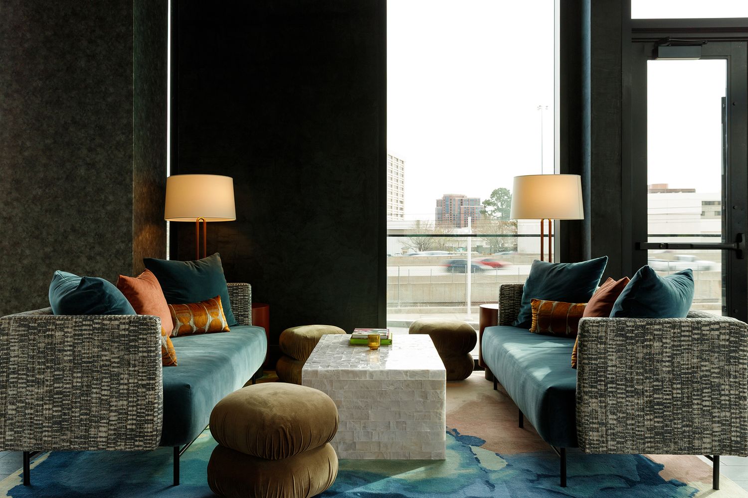 Hotel lounge with teal velvet chairs, warm lamp lighting, colorful pillows, and a marble coffee table. Interior photographer in Denver.