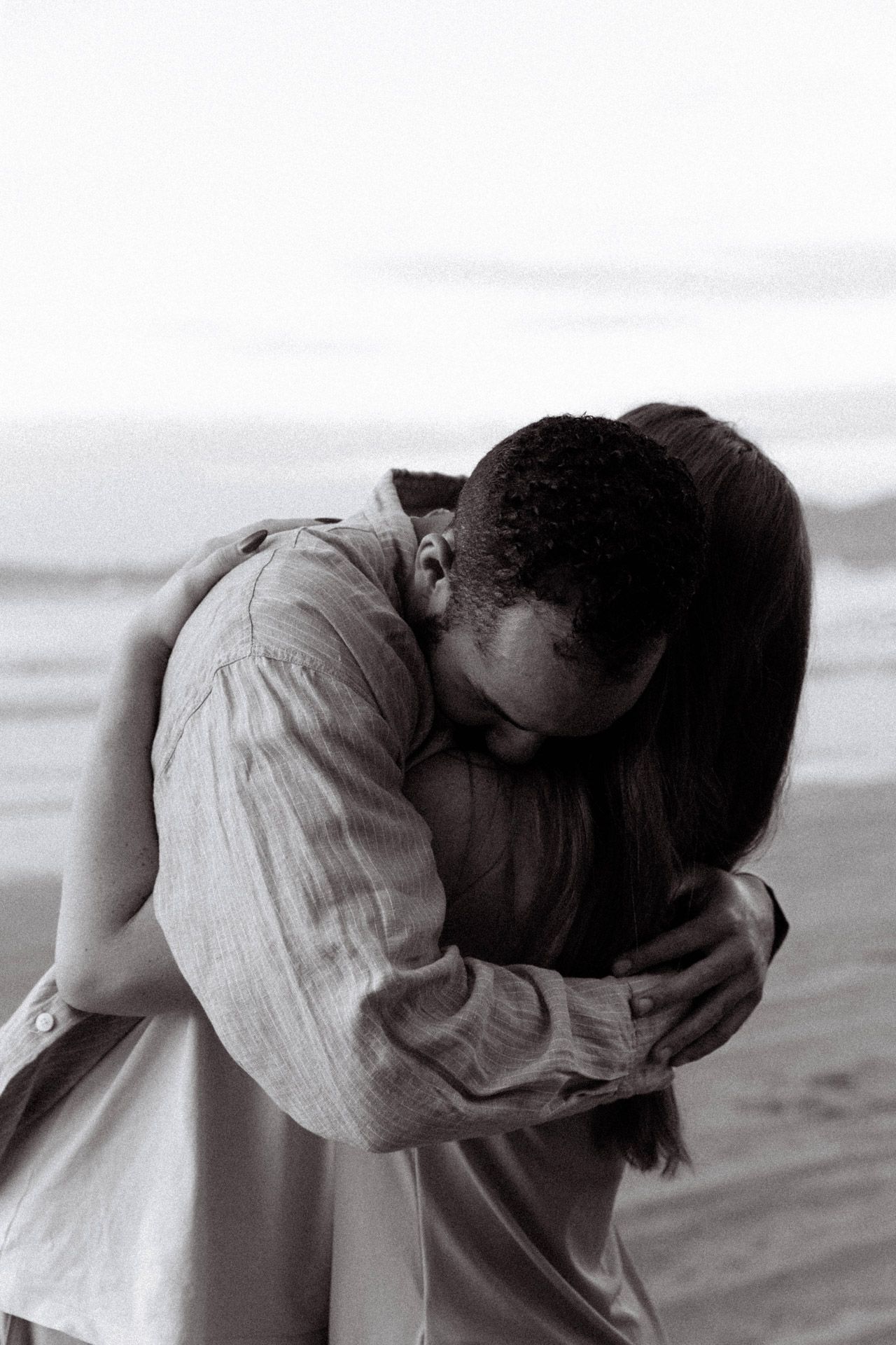 An intimate black and white photo of a couple sharing a tender moment on the beach.
