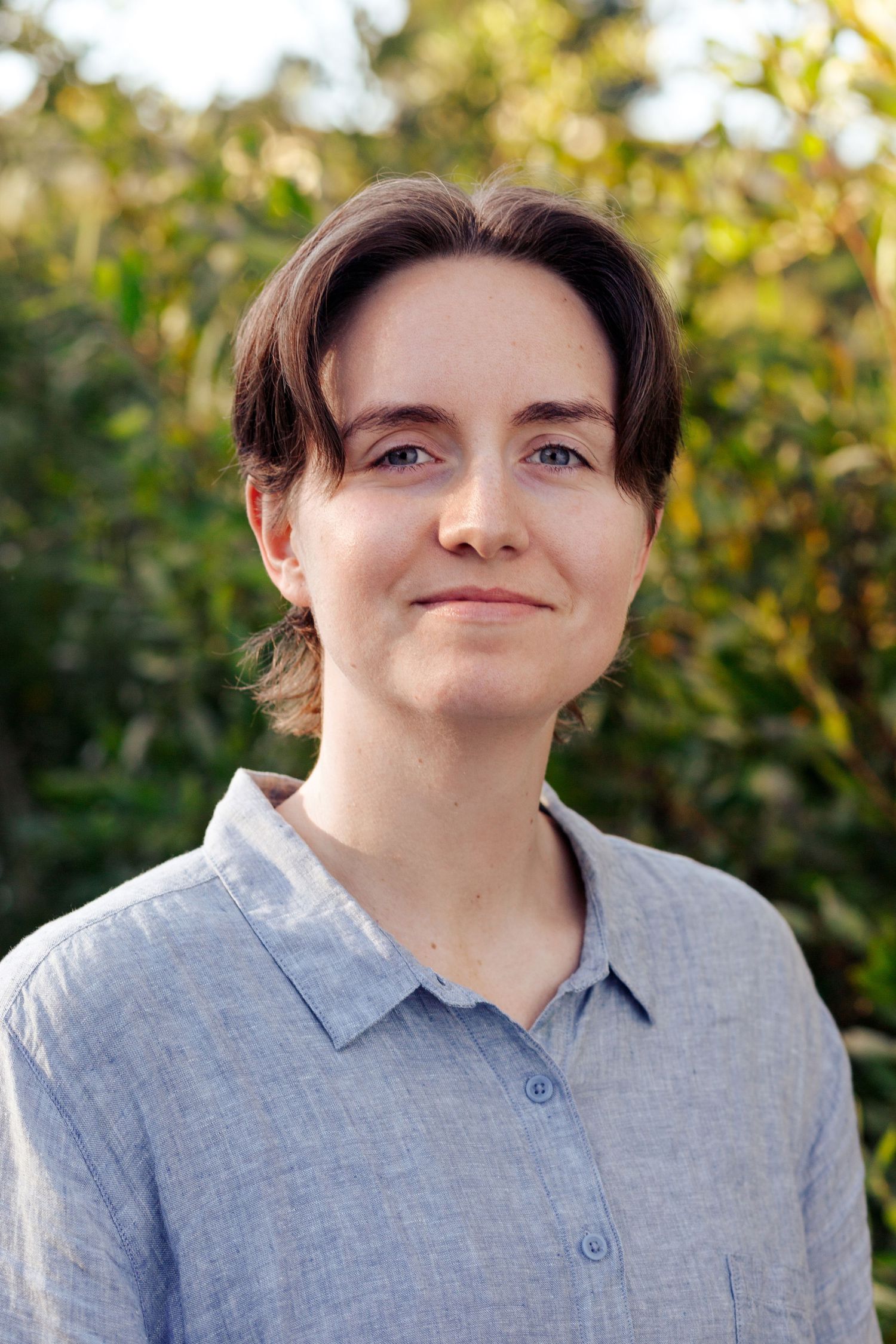 Person in a light blue collared shirt shown in a series of outdoor portraits with natural lighting and foliage background.