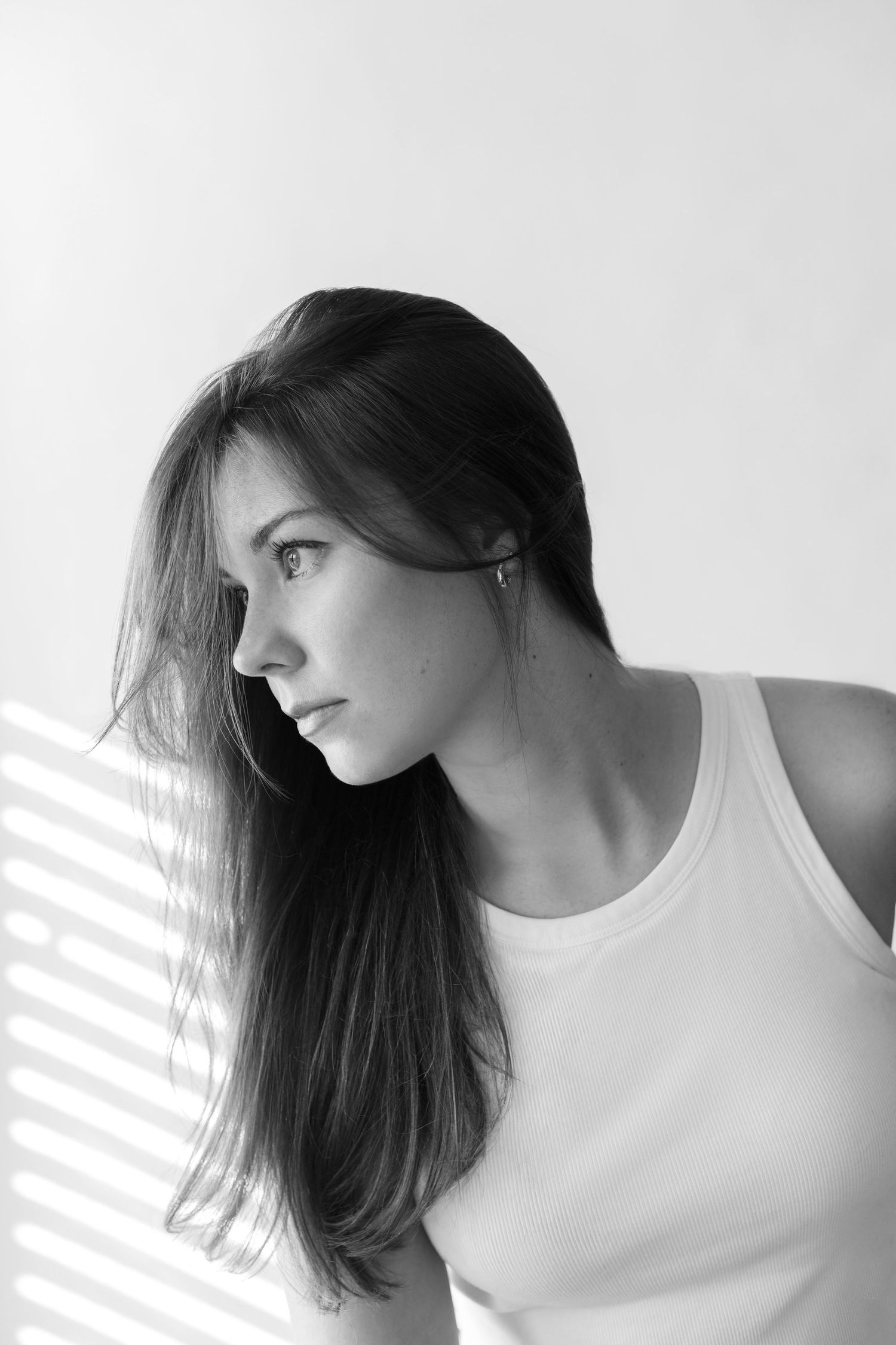 A black and white triptych showing a person with long dark hair in a white top looking to the side in three poses.