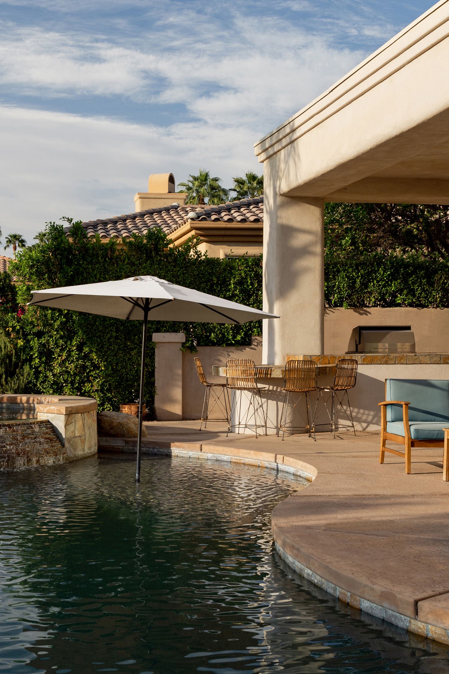Luxurious poolside patio area with covered seating, umbrellas, and stone features at a Mediterranean-style villa.