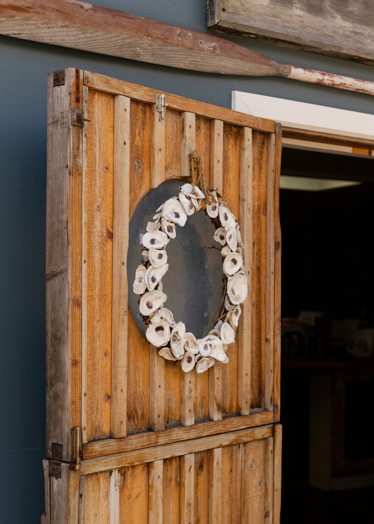 Oyster shell wreath hanging on rustic wooden barn doors with gray siding backdrop.