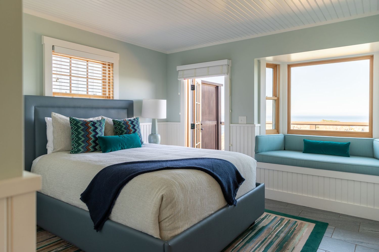 Coastal-inspired bedroom features beadboard ceiling, seafoam green walls, and white trim with natural lighting.