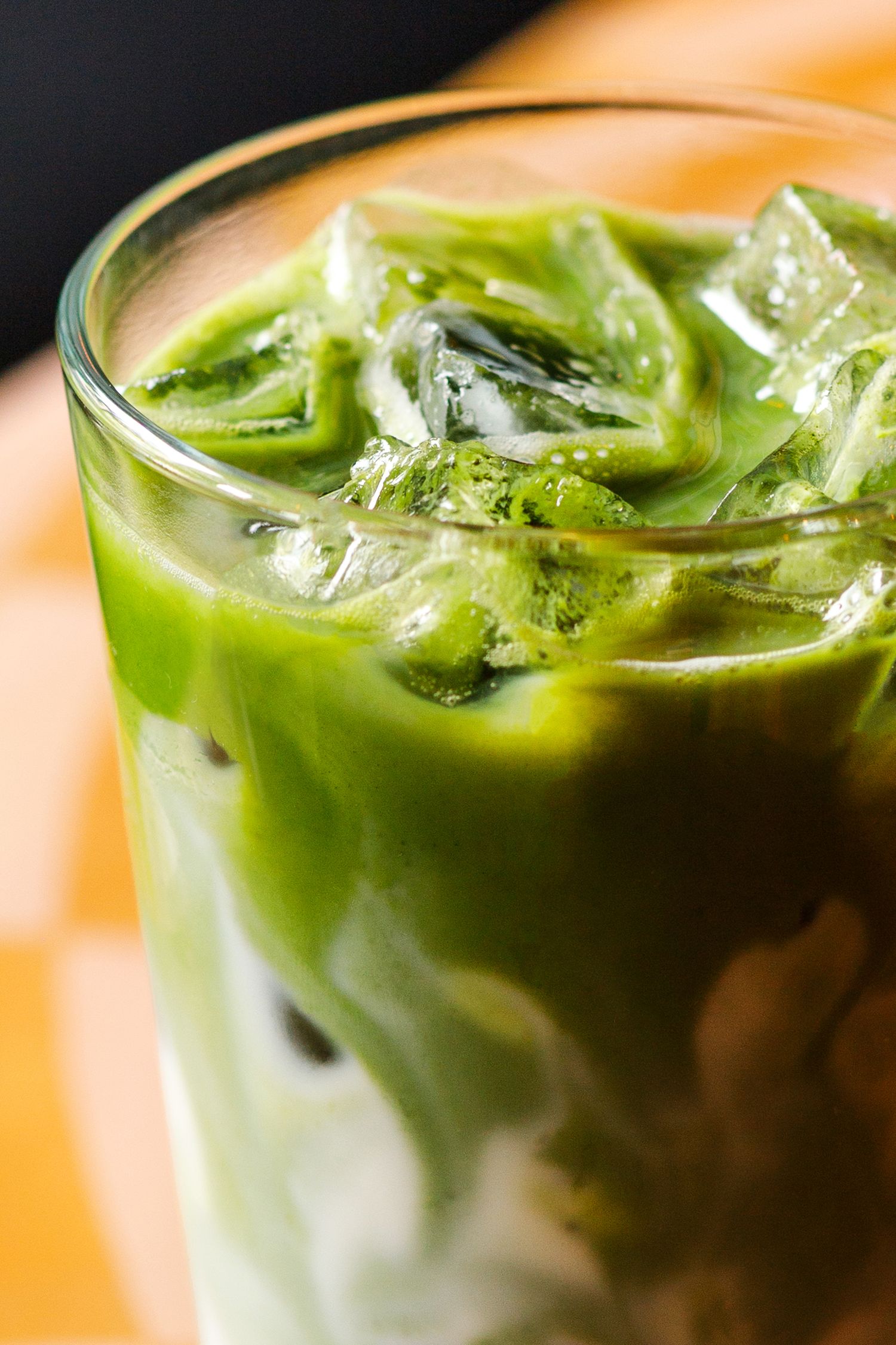 Close-up of an iced matcha green tea latte in a glass with ice cubes and swirling milk. Hospitality photography in Denver, Colorado.