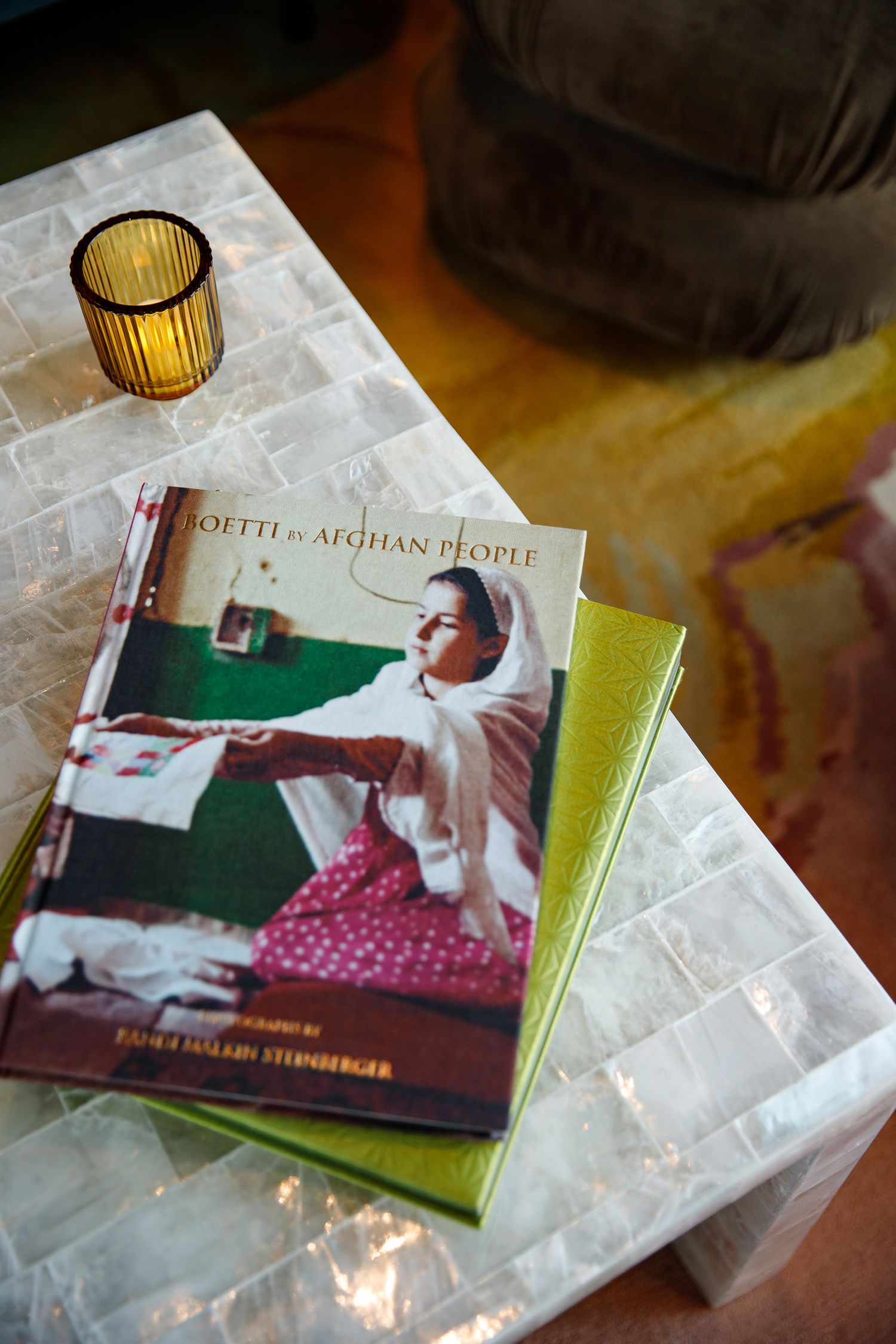 Books stacked on a white mosaic coffee table with an amber glass candle holder. Detail image by hospitality photographer based in Denver.