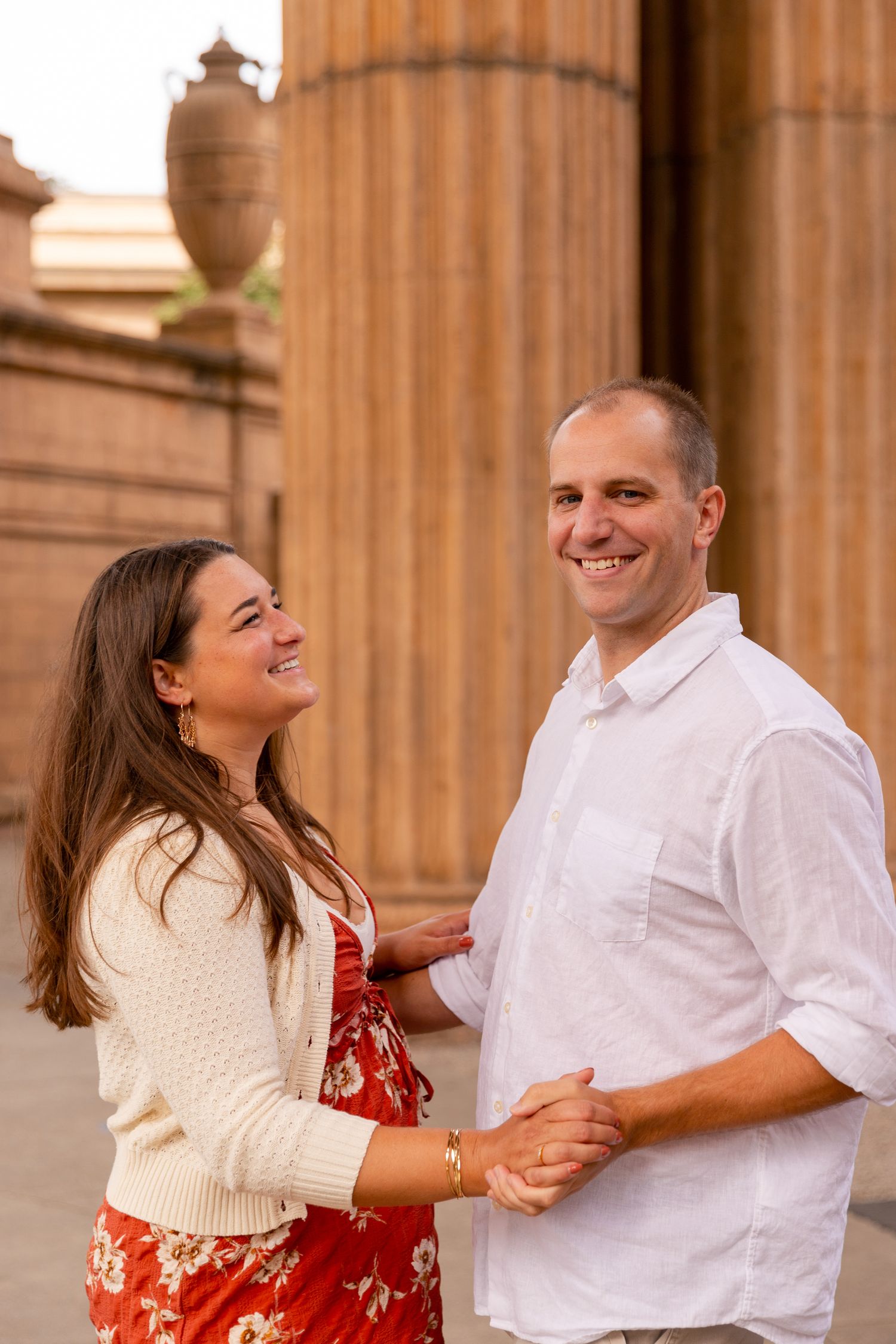 A couple dances and laughs together in front of classical stone columns during a romantic photoshoot.
