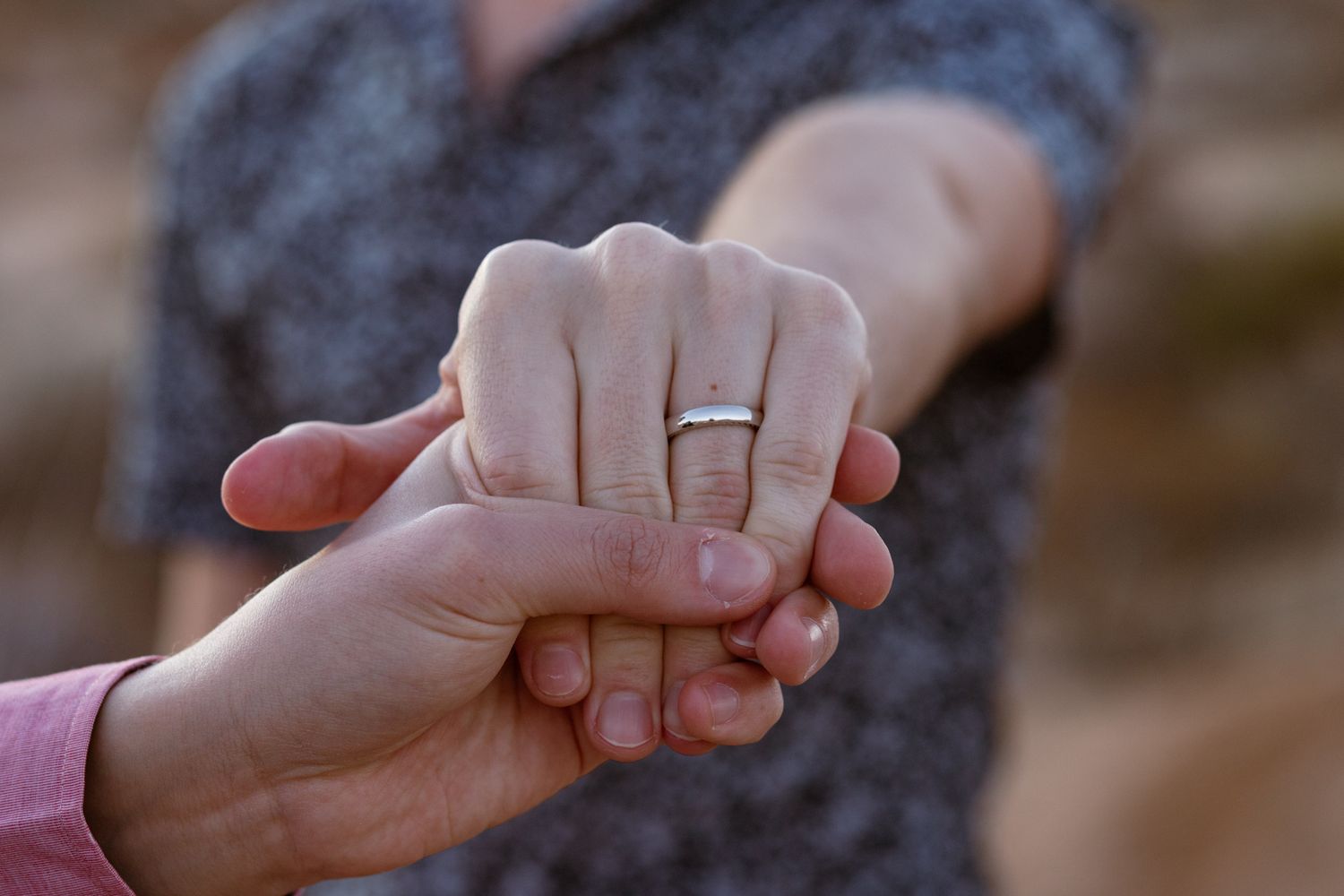 Close-up of hands with wedding rings making a heart shape against a blurred desert background.