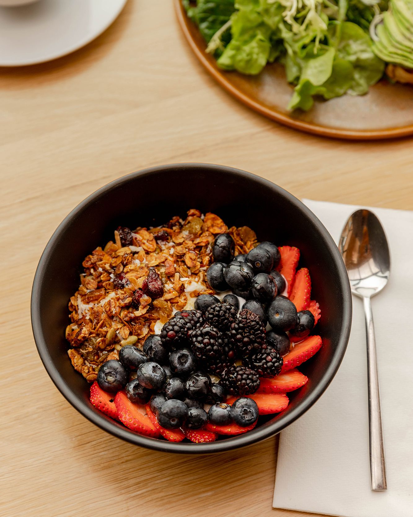 A healthy breakfast bowl filled with granola, fresh berries including blueberries, blackberries and strawberries in a black bowl.