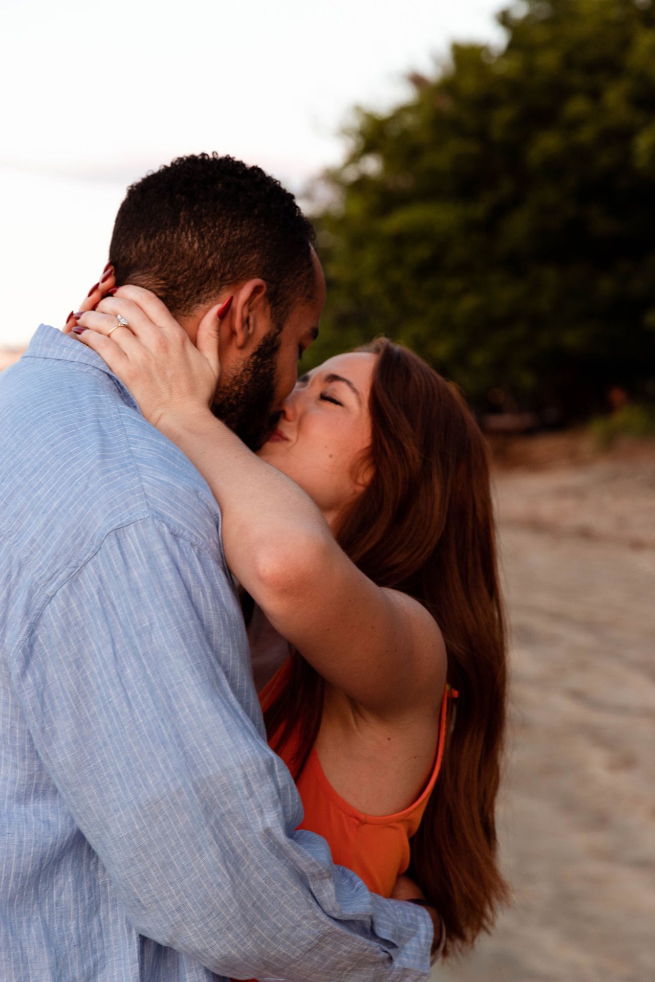 A romantic couple embraces and kisses on a beach during golden hour.