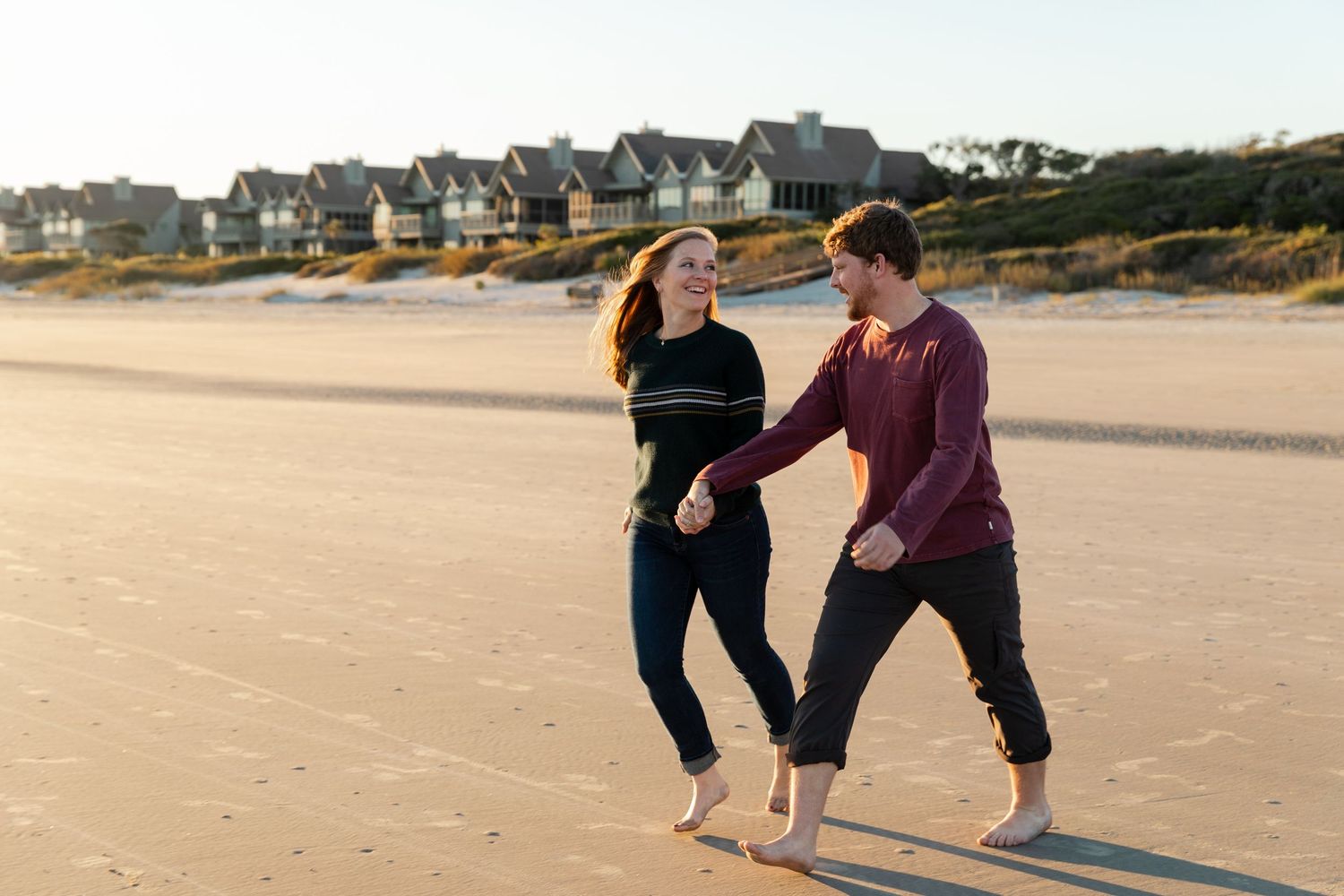 Two people practicing yoga poses together on a sandy beach at sunset.